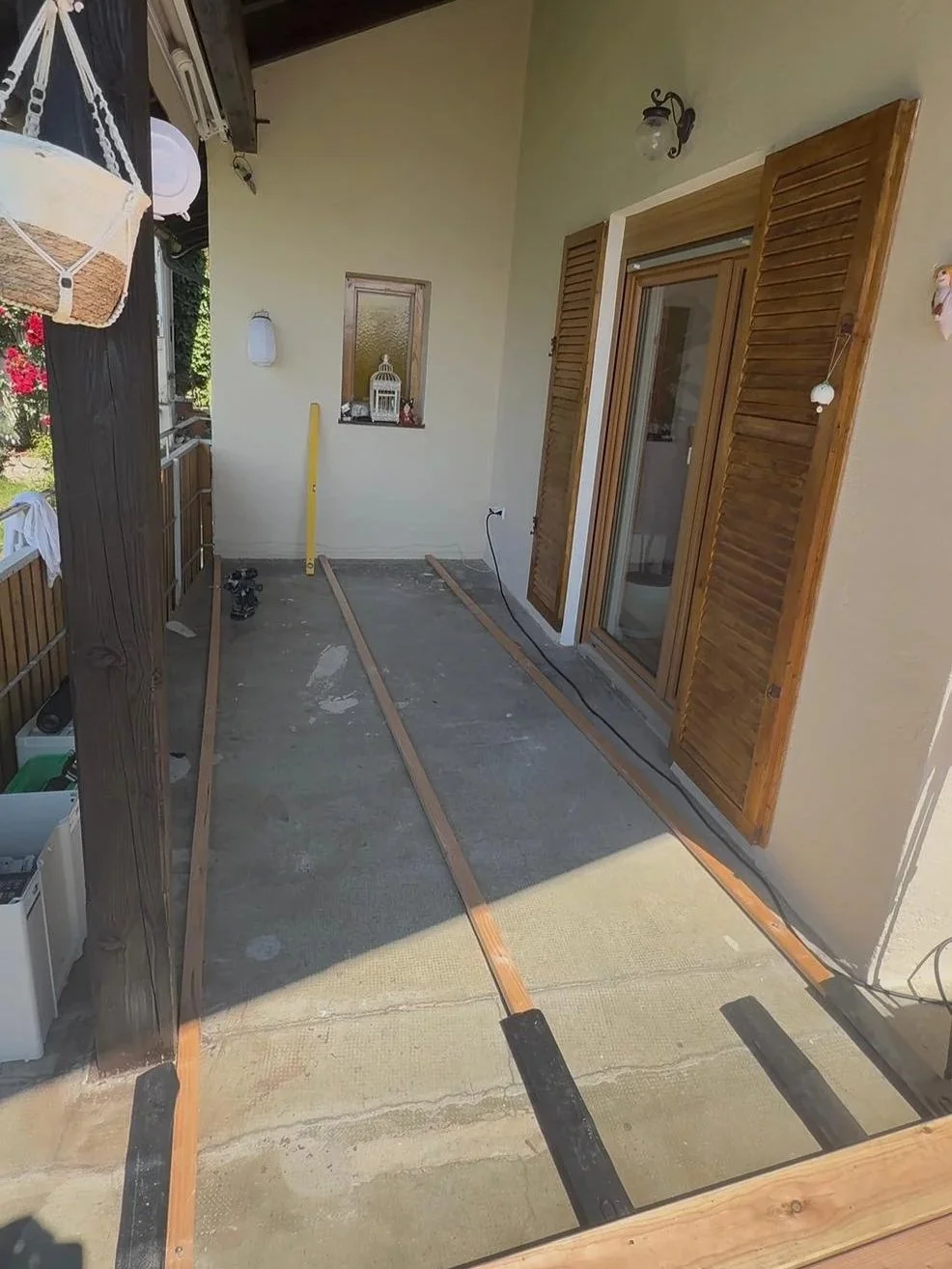 Ein Balkon mit offenen Holzbalkonläden, Bauarbeiten im Gange, die Bodenplatte ist vorbereitet, um eine Terrasse zu legen, mit einigen Werkzeugen und Baumaterialien.