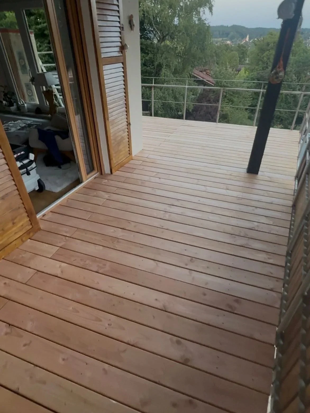 Leerer Holzpersonenbalkon mit Blick auf grüne Bäume und eine Stadt im Hintergrund.