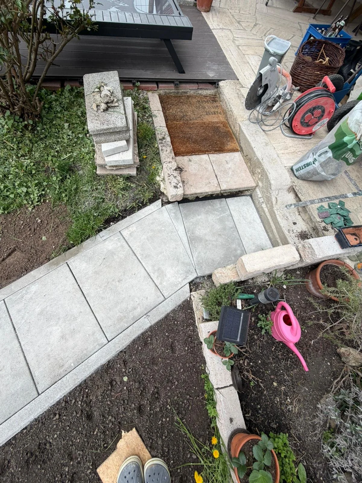 Gartenarbeiten im Bereich einer Terrasse, Arbeiten an der Terrassenbuchten und Pflasterung, mit Werkzeug und Baumaterialien.