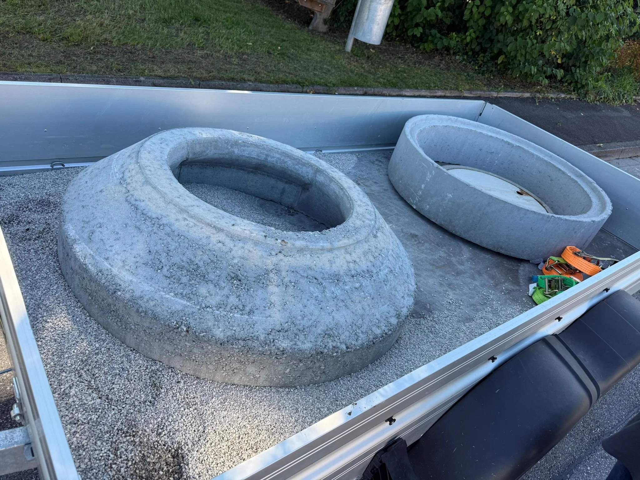 Zwei runde Betonkonstruktionen auf einem Bauwagen, vermutlich Tierkotschüsseln. Es liegen Werkzeuge und Sicherheitsbänder daneben.