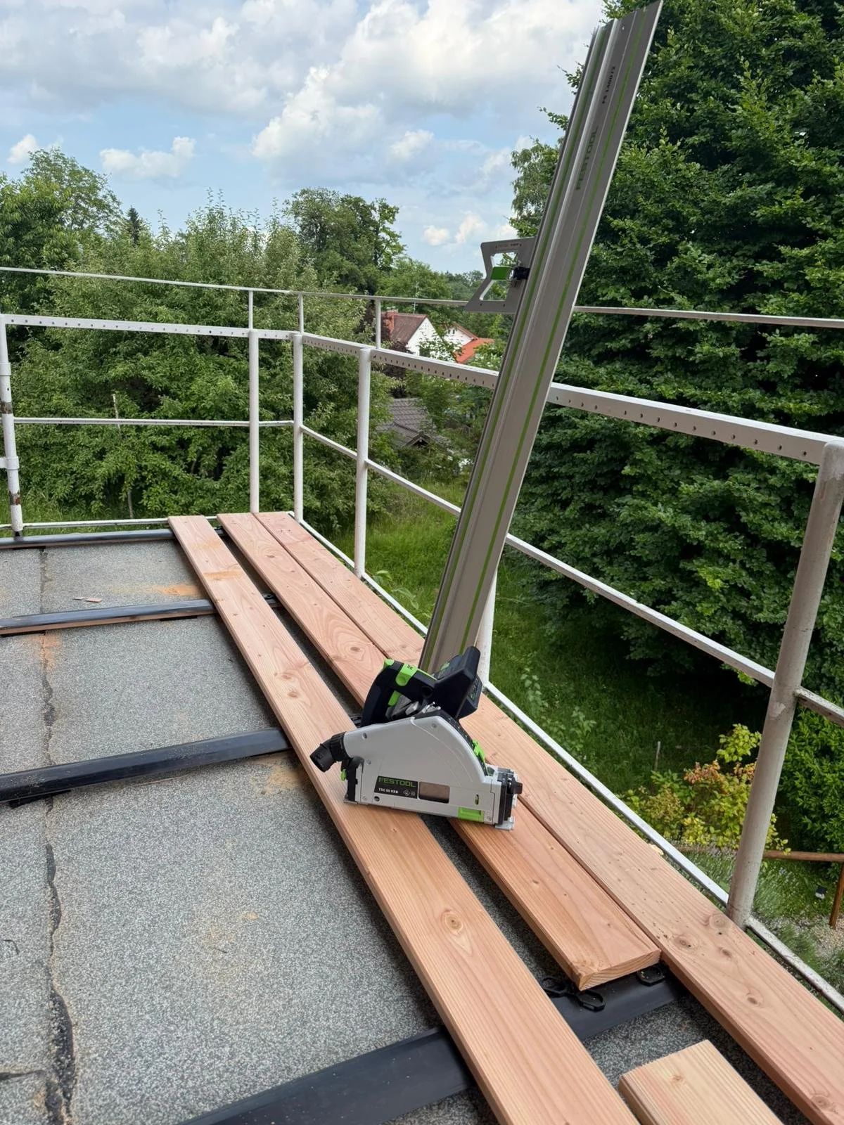 Bauarbeiten auf einer Dachterrasse mit Holzlatten, eine elektrische Stichsäge und eine Leiter.