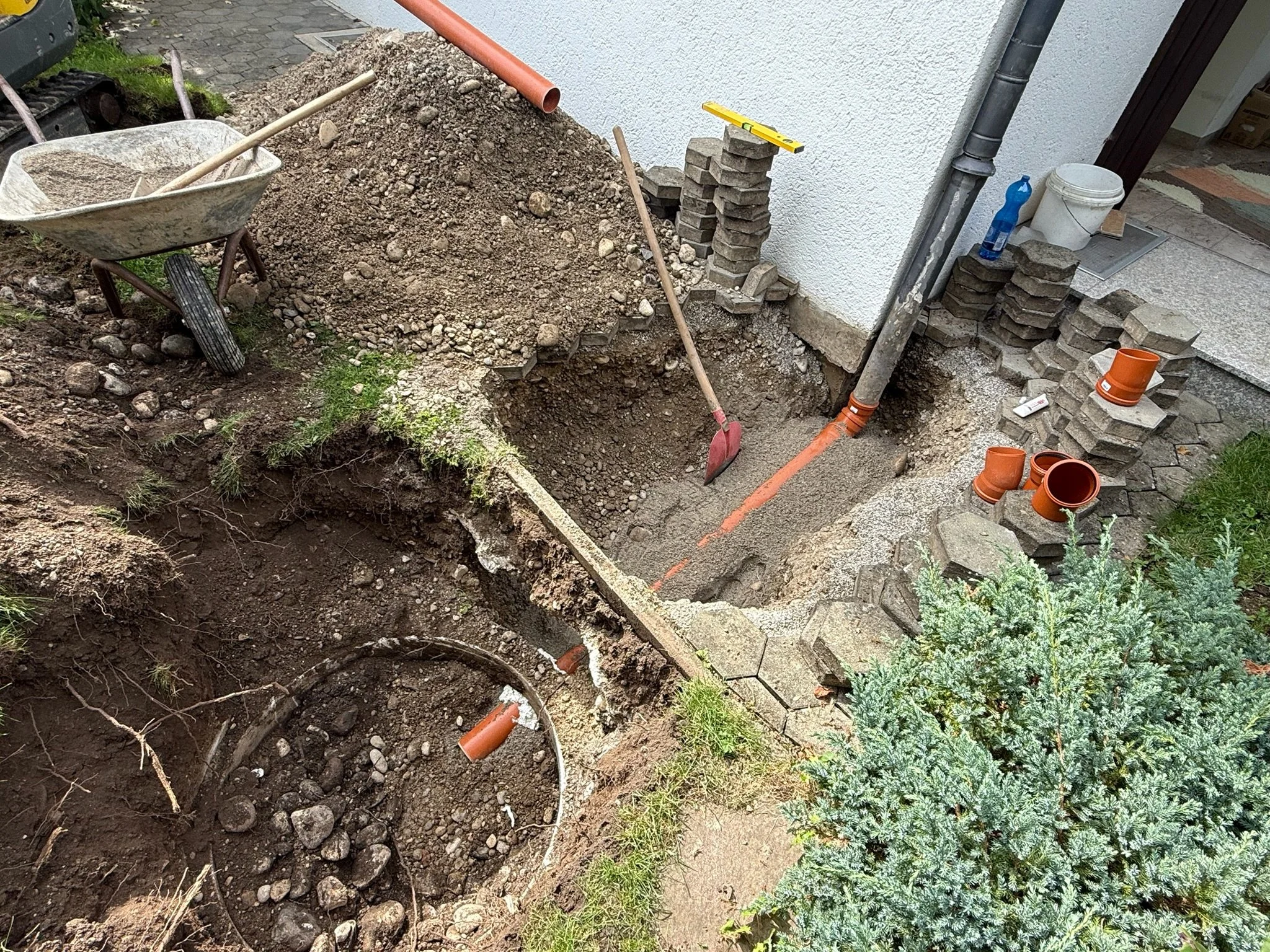 Bauarbeiten am Fundament eines Hauses, mit Schaufel, Betonsplitt, Pflastersteinen, Rohren und Baustoffen