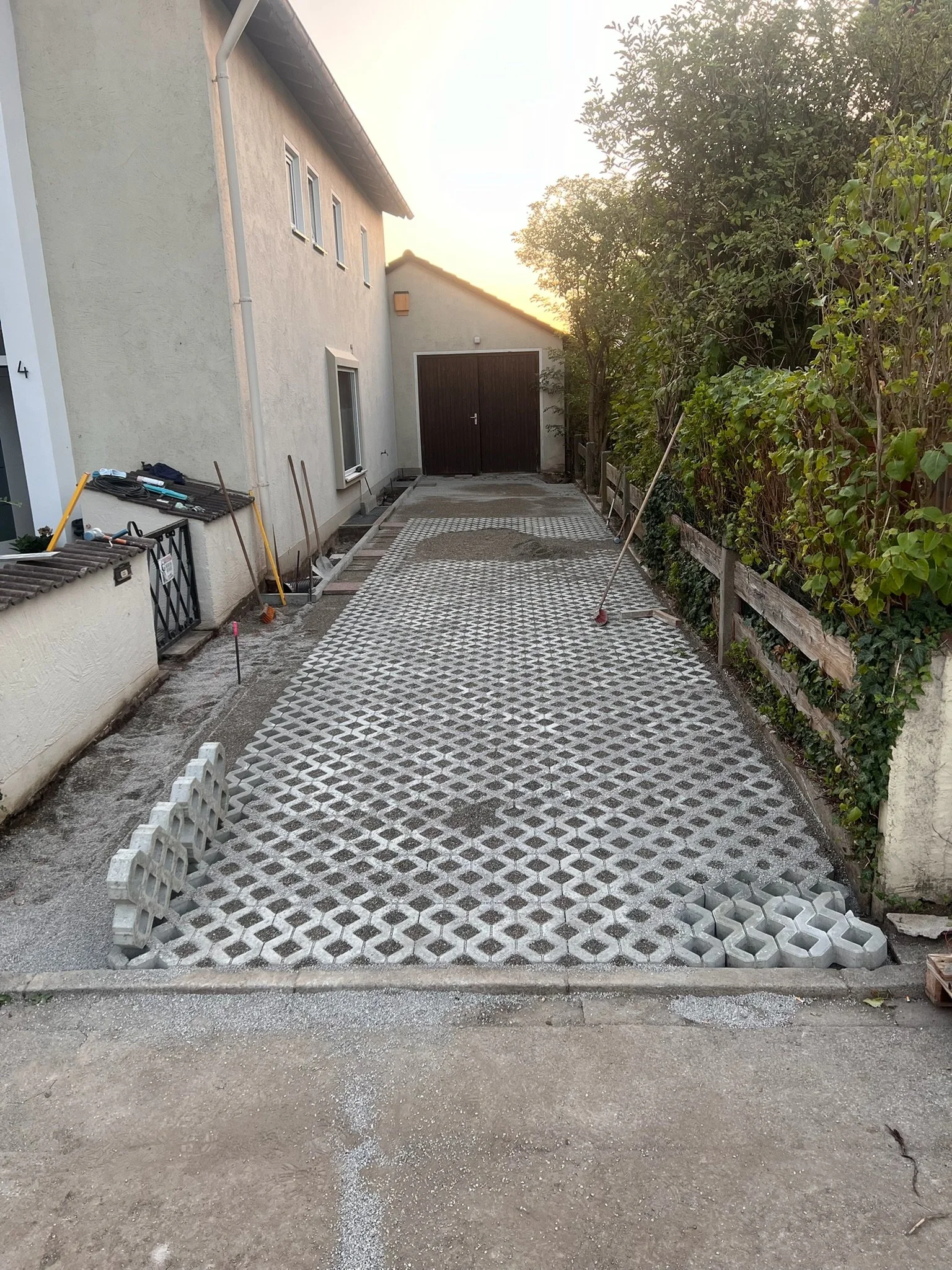 Der Gehweg wird mit perforierten Betonpflastersteinen neu gepflastert, einige Steine sind bereits verlegt, andere liegen noch bereit. Es liegen Werkzeuge und Baumaterialien auf der Seite, die von den Bauarbeiten genutzt werden.