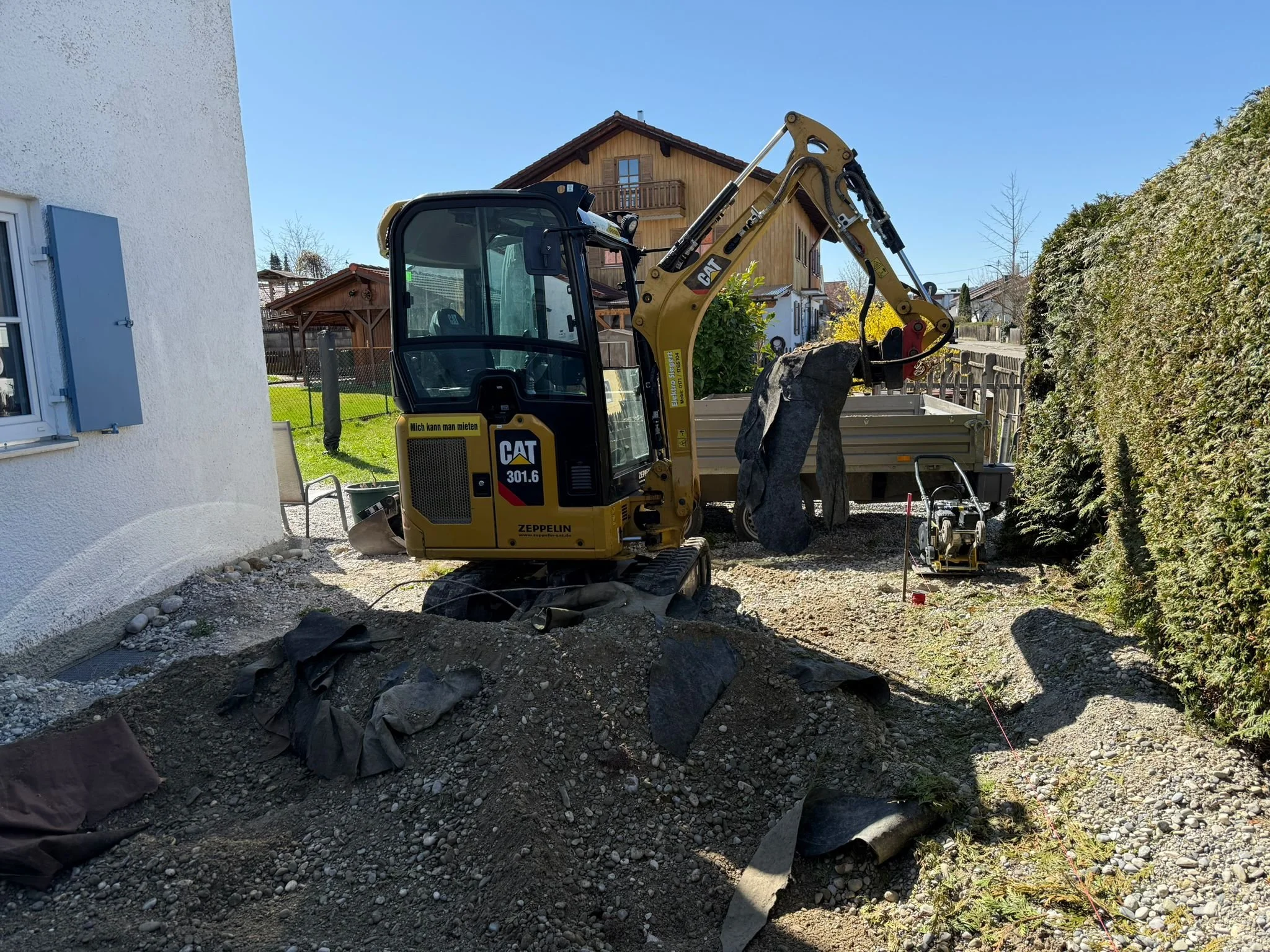 Bauarbeiten im Garten mit Minibagger, Erde und Baumaterialien
