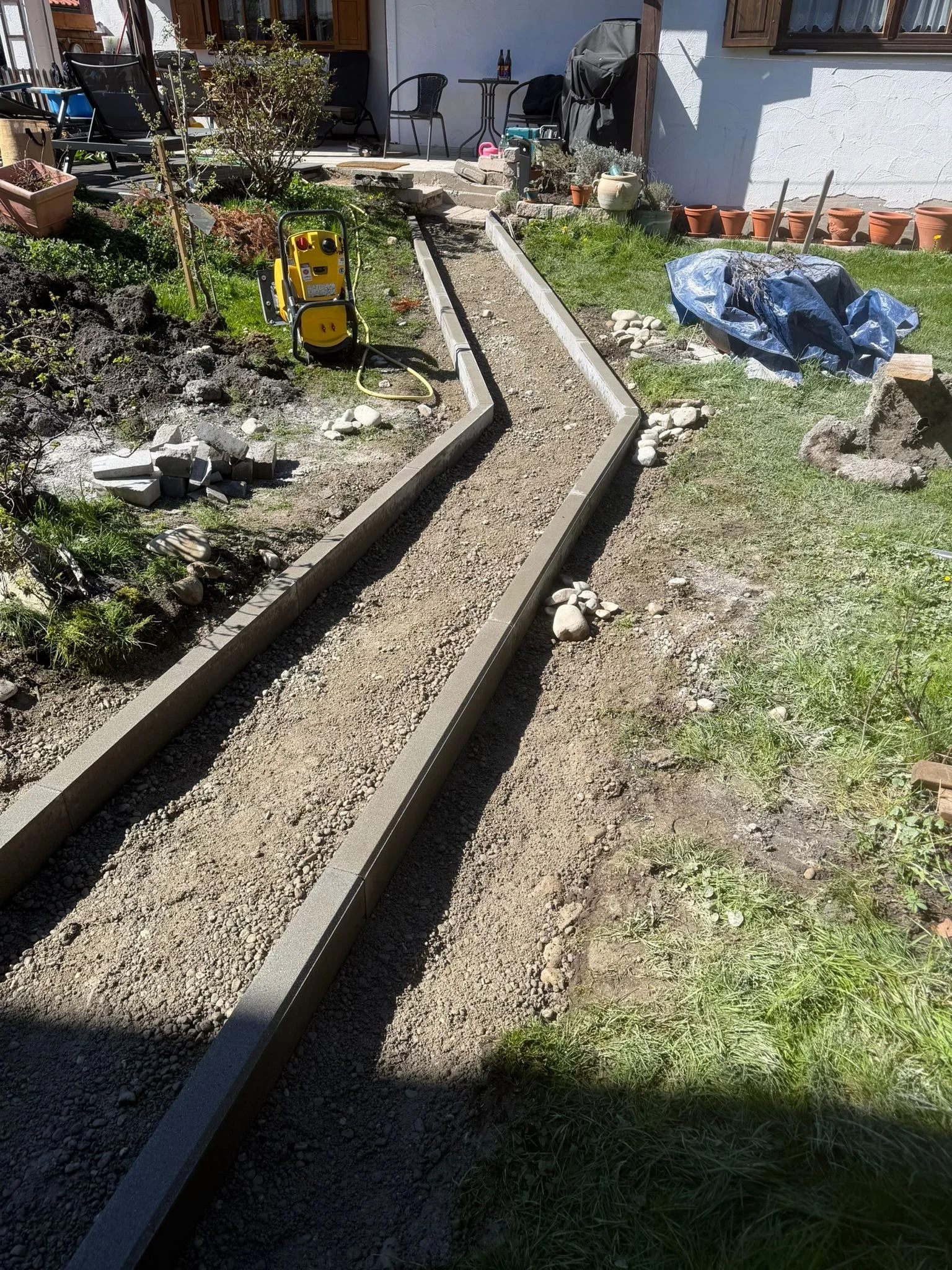 Garten wird mit Gehweg aus Pflastersteinen gebaut. Es sind Bauwerkzeuge und Materialien im Einsatz.