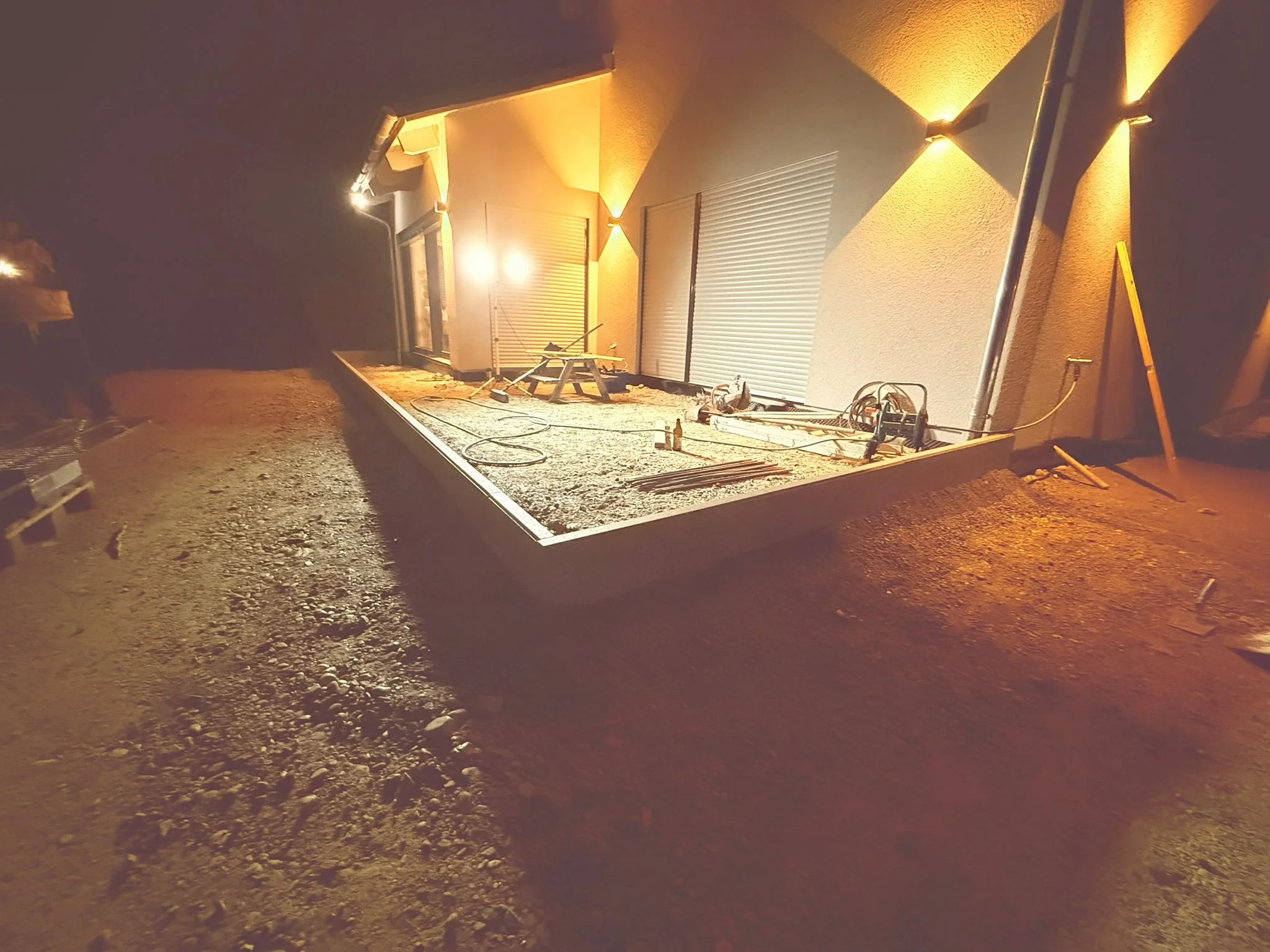 Baustelle vor einem Haus bei Nacht, mit Bauwerk und Baumarkteinrichtungen, Beleuchtung leuchtet auf die Baustelle.