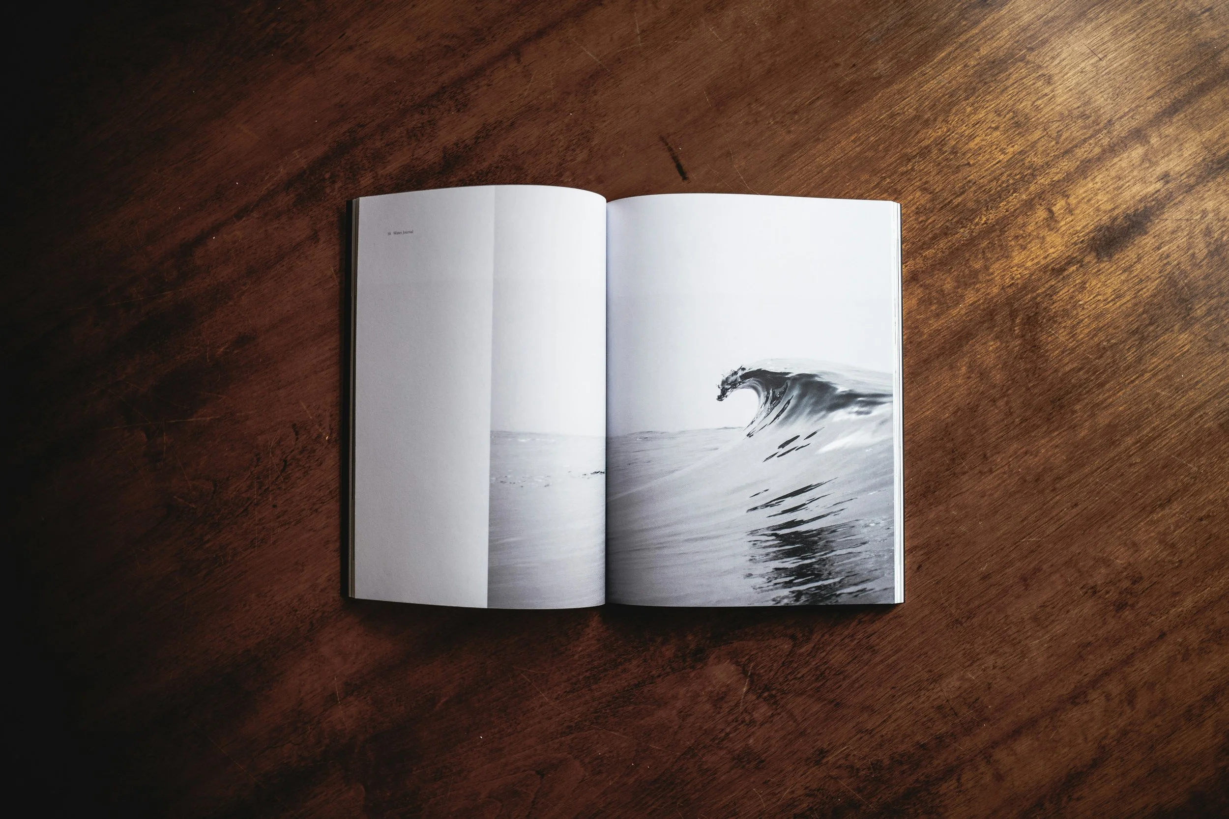 Open book with black and white ocean wave photograph on right page, placed on wooden surface.