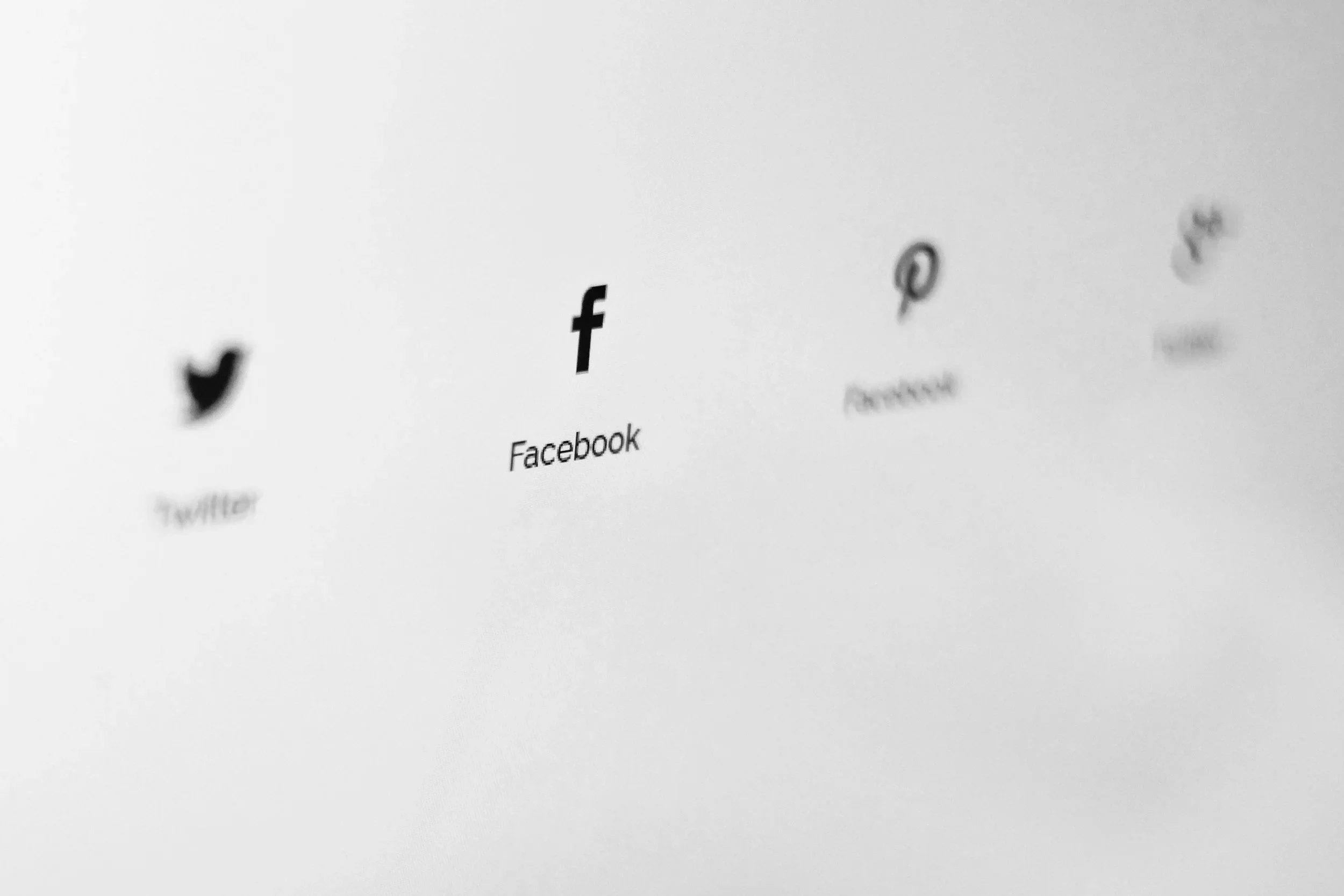 Black and white image showing social media icons for Twitter, Facebook, Pinterest, and Instagram with their names beneath, taken with a shallow focus.