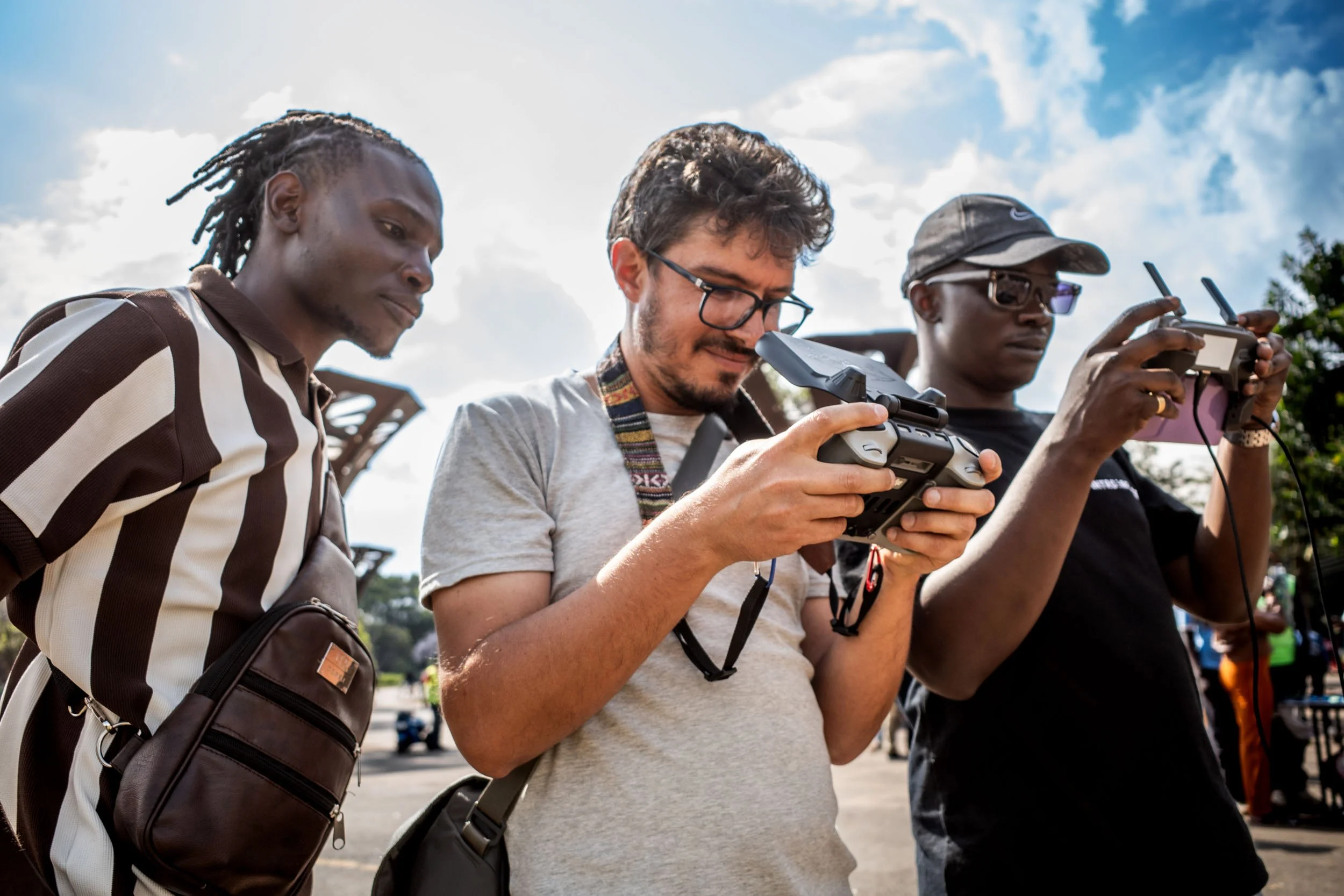 Three crew members standing outdoors, two using remote controllers and one holding a drone remote.