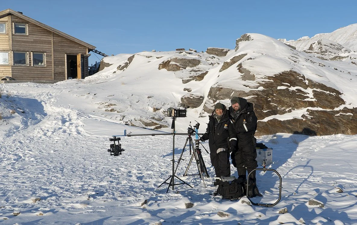 Thought Leader on production in the snow with camera equipment, mountains and a wooden building in the background.