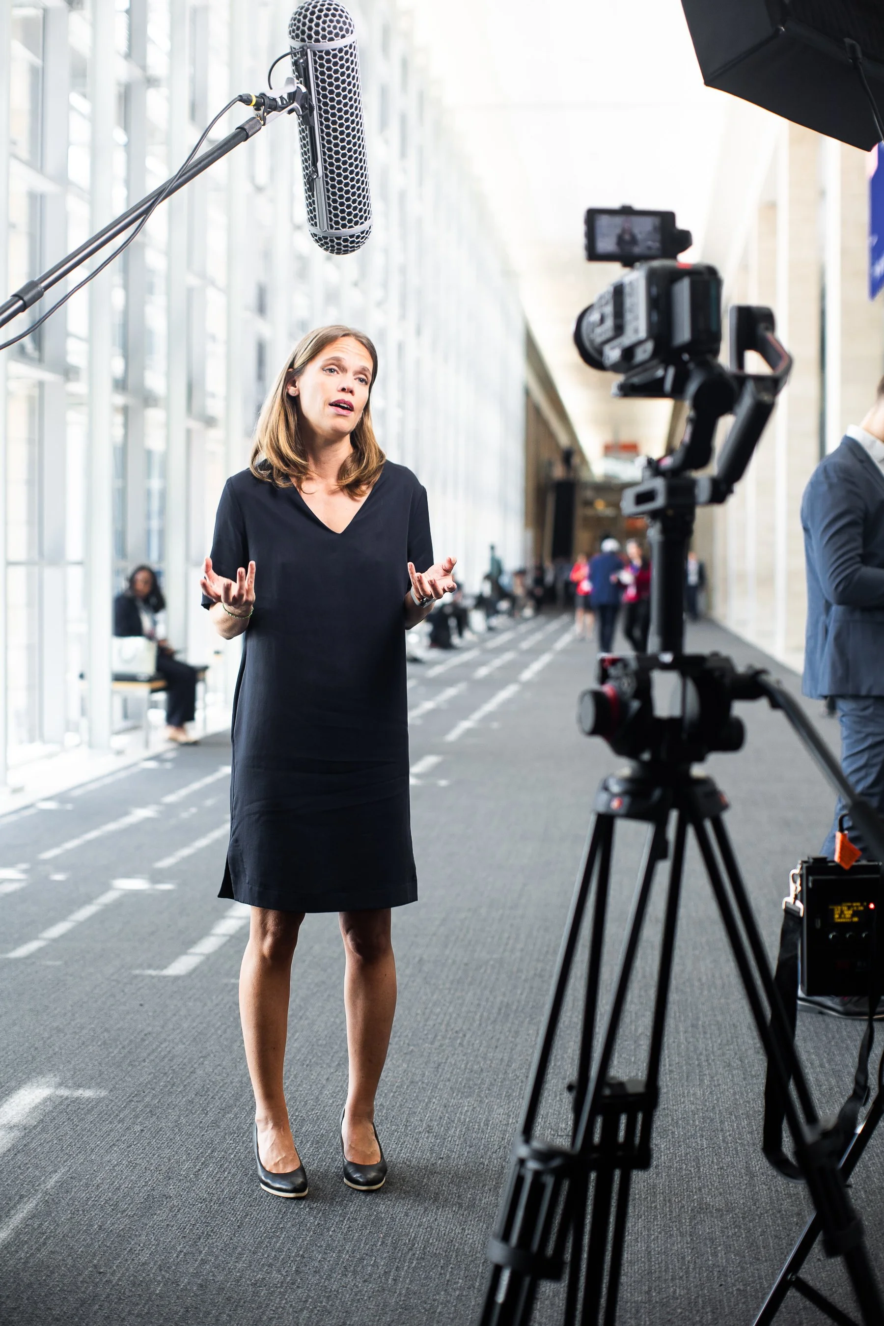 Finnfund member on a black dress is speaking or giving an interview in front of a camera at a professional setting, AfricaTech Festival in Cape Town, with a microphone overhead and several people in the background.