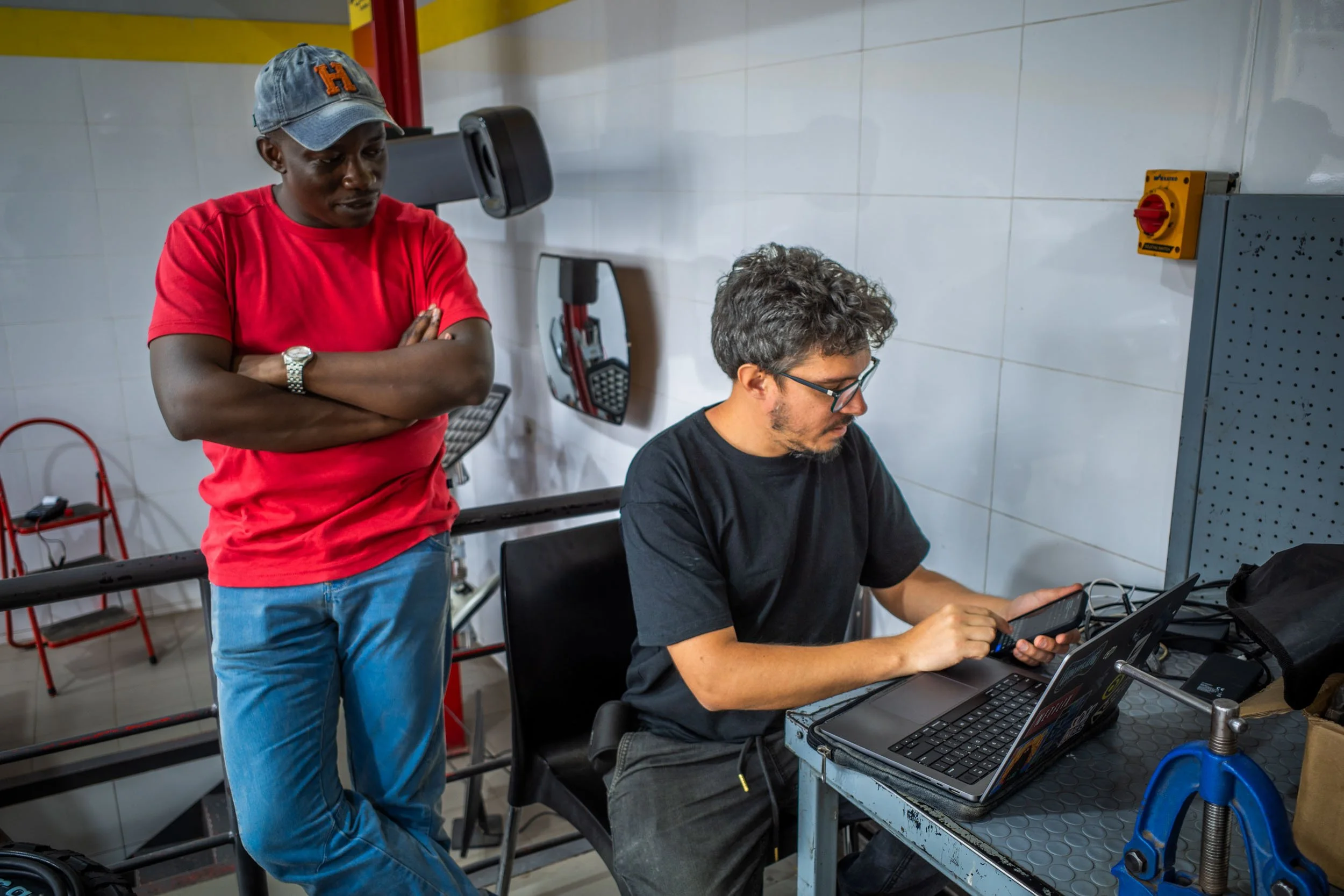 Thought Leader crew working in a garage, one seated at a desk with a laptop and the other standing nearby, looking at a device.
