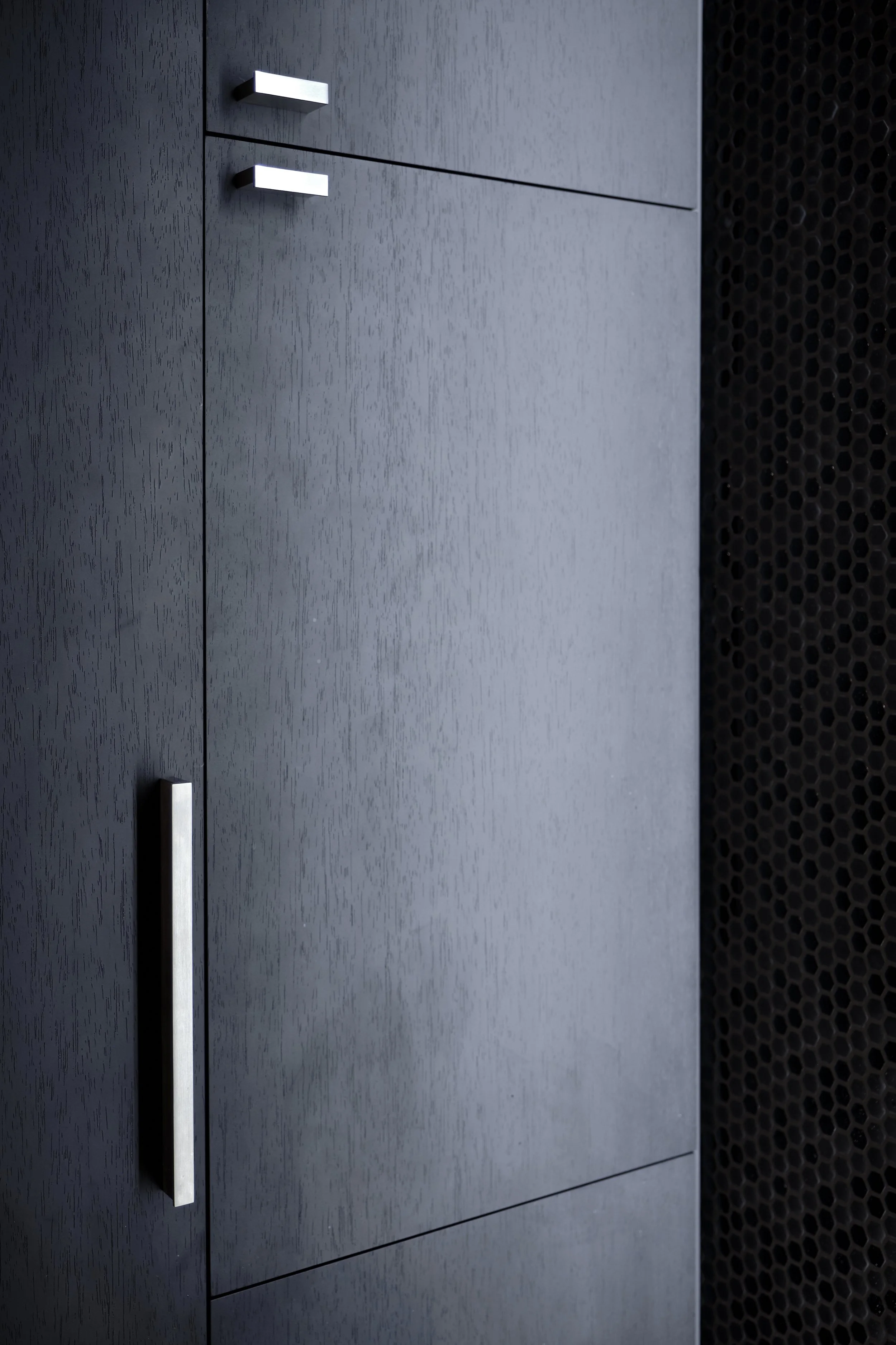 Close-up of a modern, dark gray wooden cabinet with silver handles, with a black, honeycomb-patterned surface on the right side.