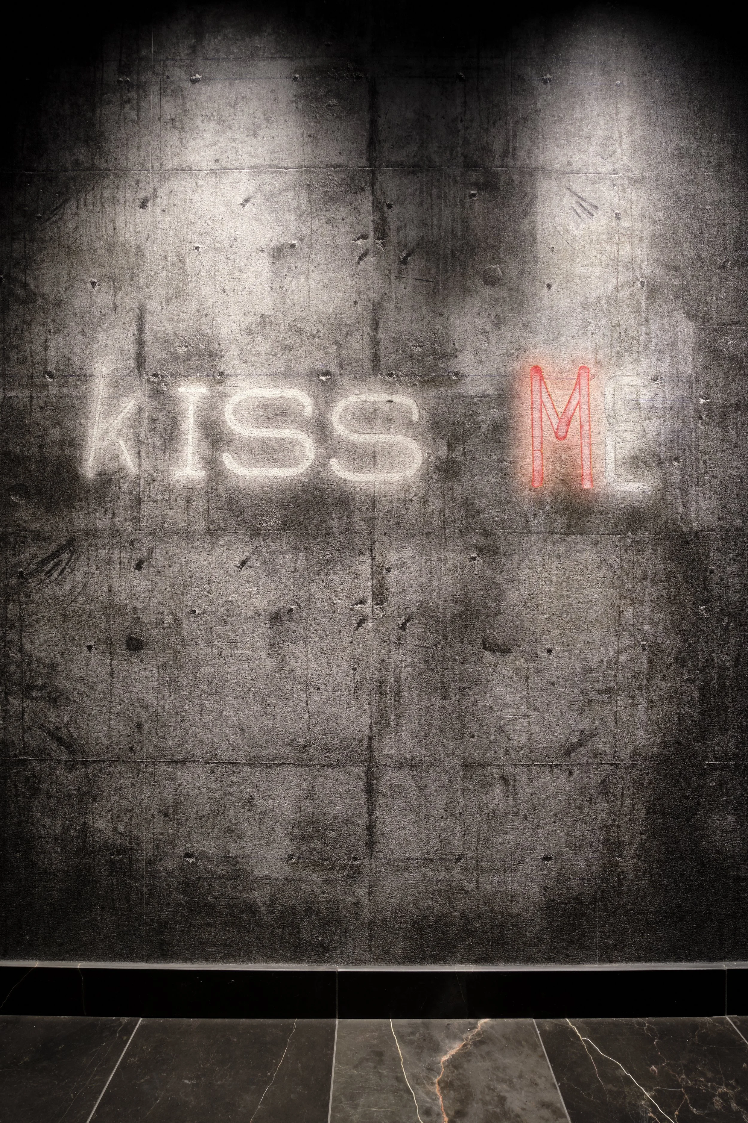 Neon sign on a concrete wall that reads 'KISS ME' with 'KISS' in white and 'ME' in red.