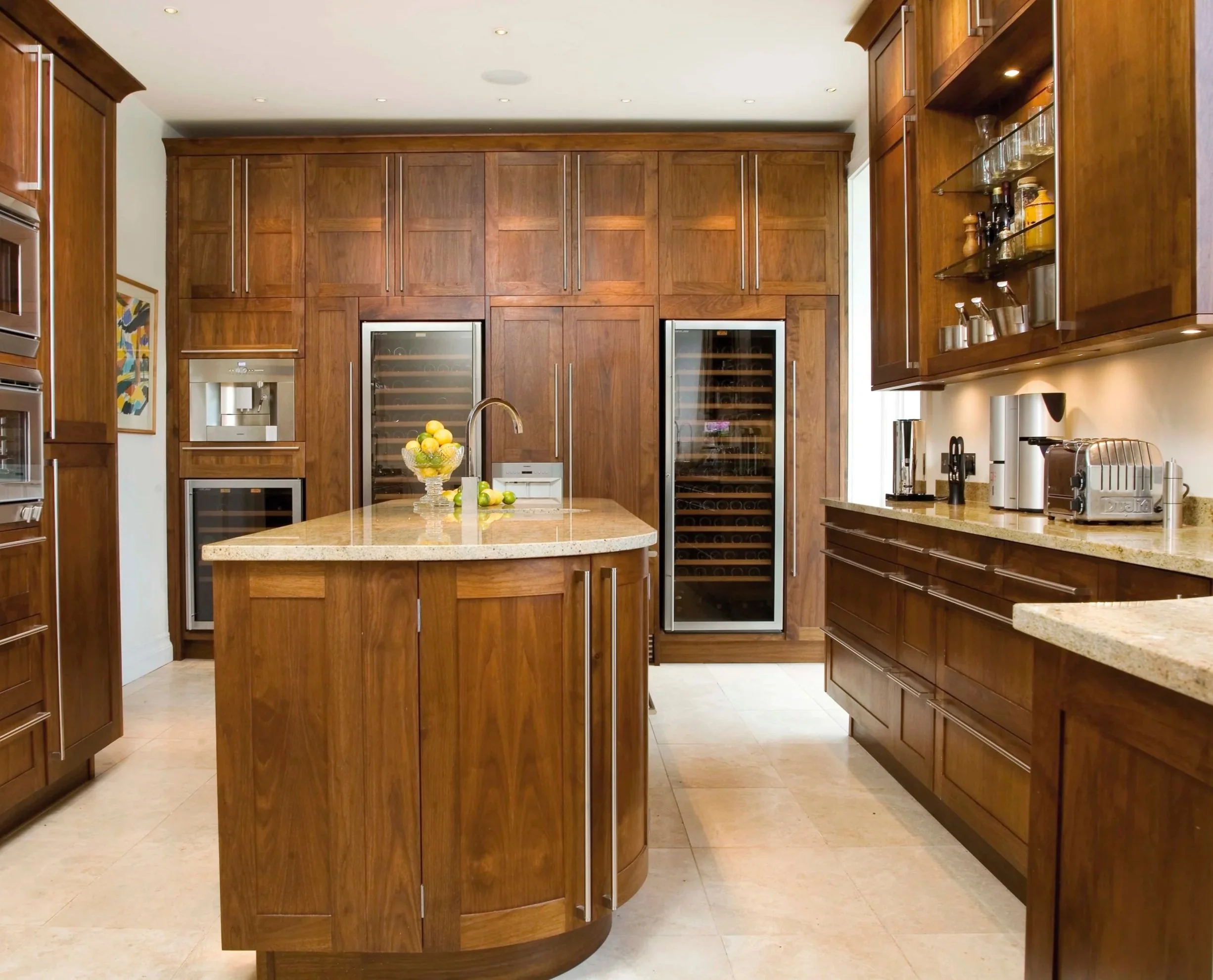 Modern kitchen with wooden cabinets, beige countertops, two wine refrigerators, and a small island with a bowl of lemons.