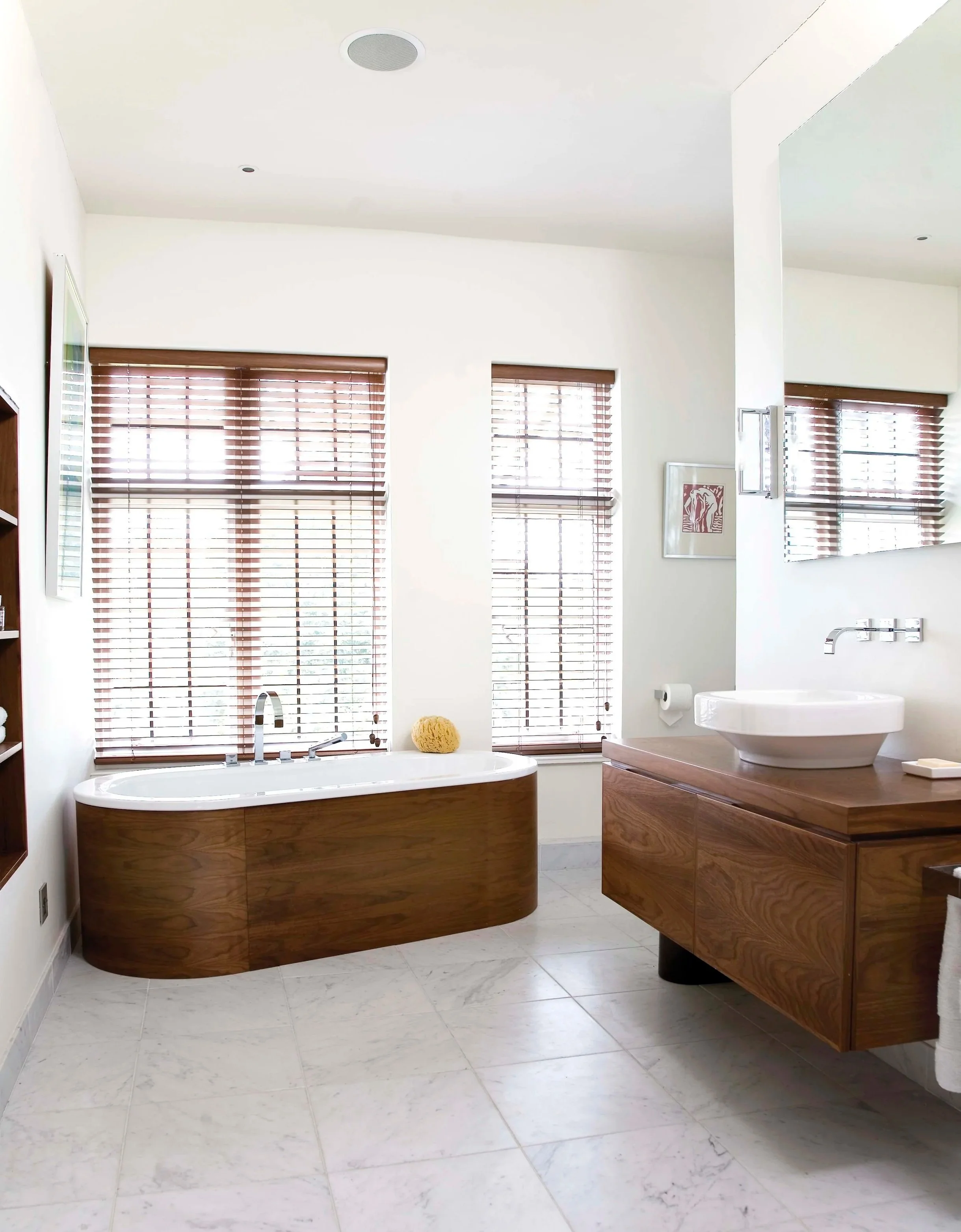 Modern bathroom with large mirror, wooden vanity, vessel sink, white bathtub, and wooden blinds on windows.
