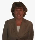 A woman with short curly brown hair, smiling, wearing a beige blazer over a white top.