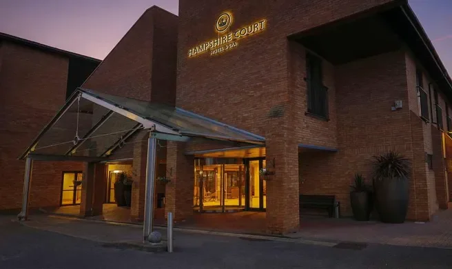 Exterior of Hampshire Court building at dusk with glass entrance, wooden door, and potted plants outside.