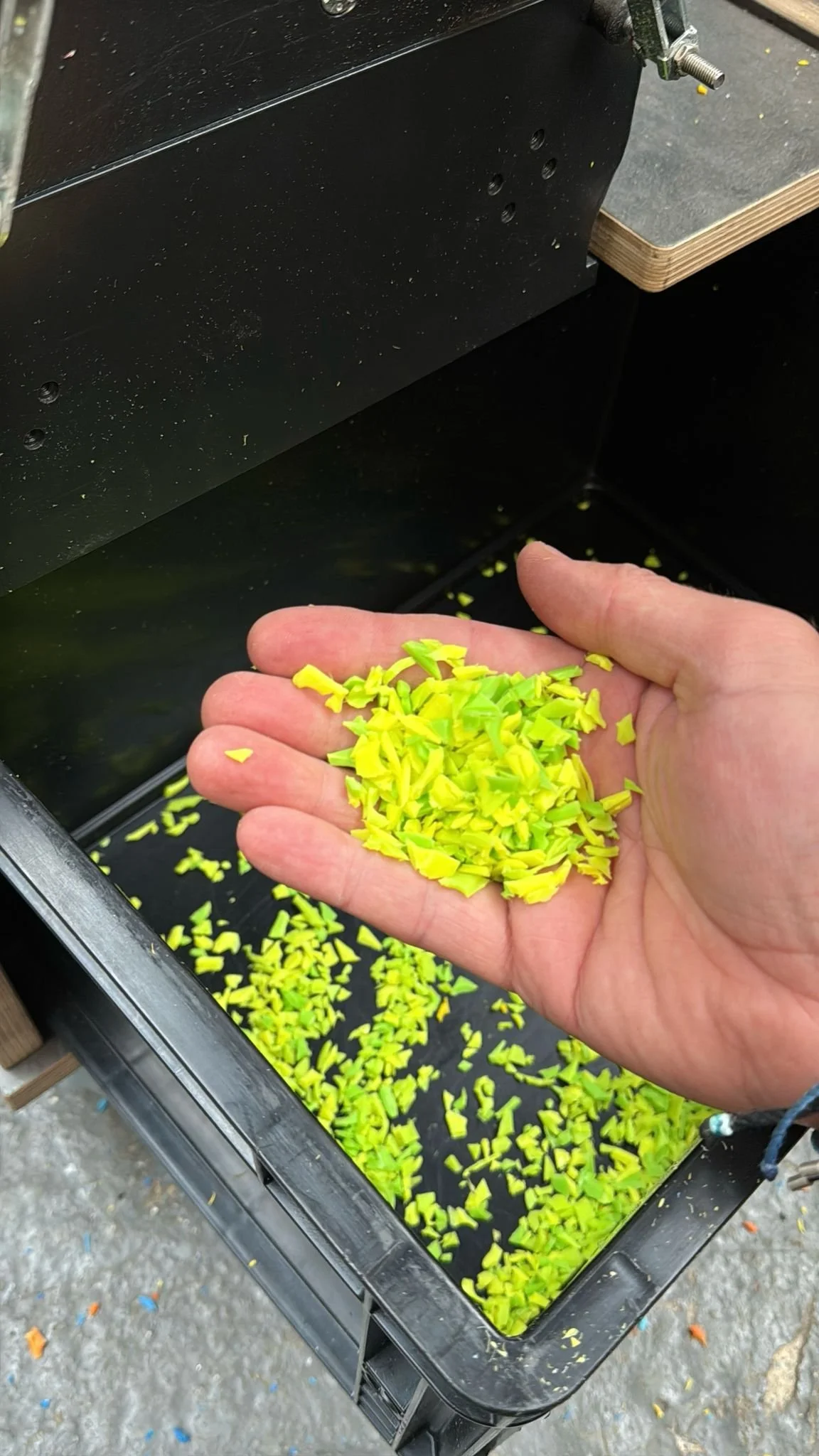 A person's hand holding small yellow plastic or paper fragments over a black container filled with similar fragments.