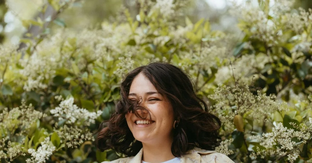Lächelnde junge Frau im Freien vor blühenden Pflanzen