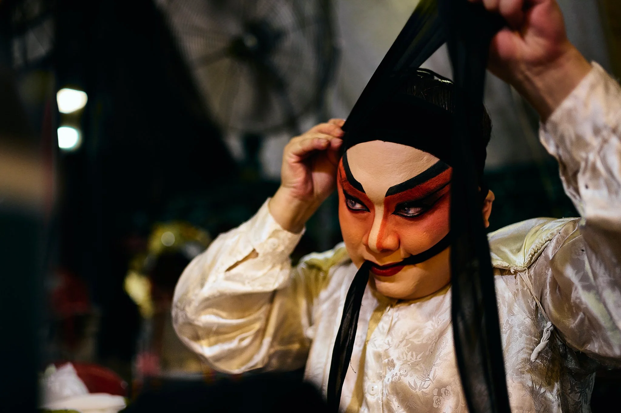 Chinese opera performer adjusting headpiece backstage before a performance.