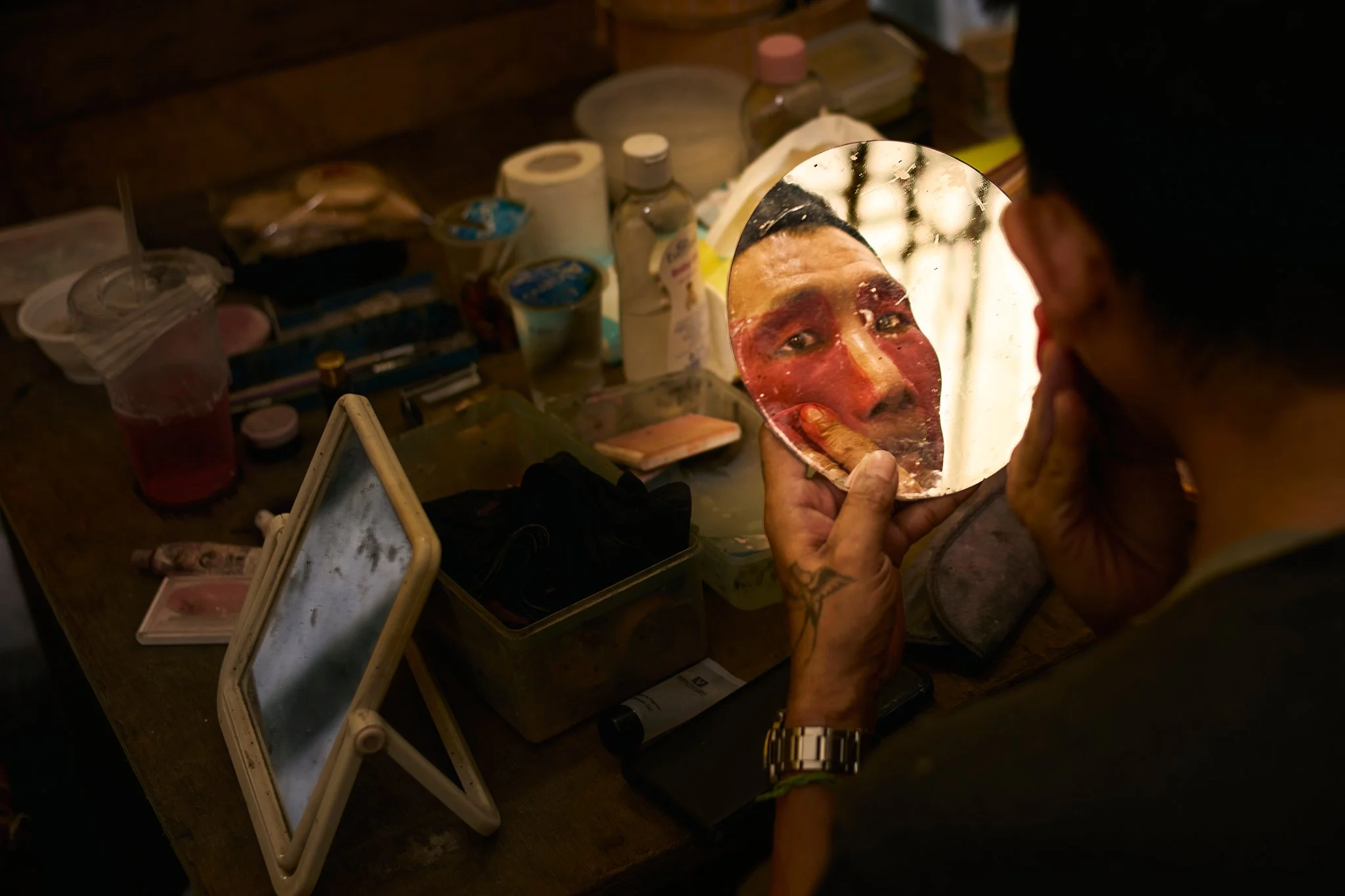 A Chinese opera performer applies makeup in front of a mirror, caught in a moment of reflection before becoming the character.