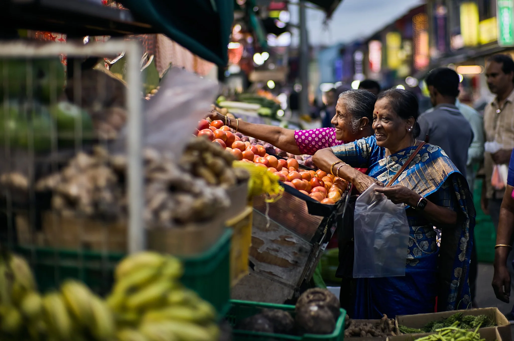 "Hands that Know" - two ladies selecting tomatos at a market, their gestures sure and unhurried. Every touch shows familiarity - a rhythm formed through years of daily life.