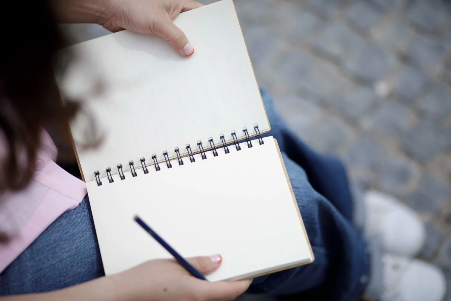 Persona sosteniendo una libreta en blanco y un bolígrafo en un entorno exterior con piso de piedra.