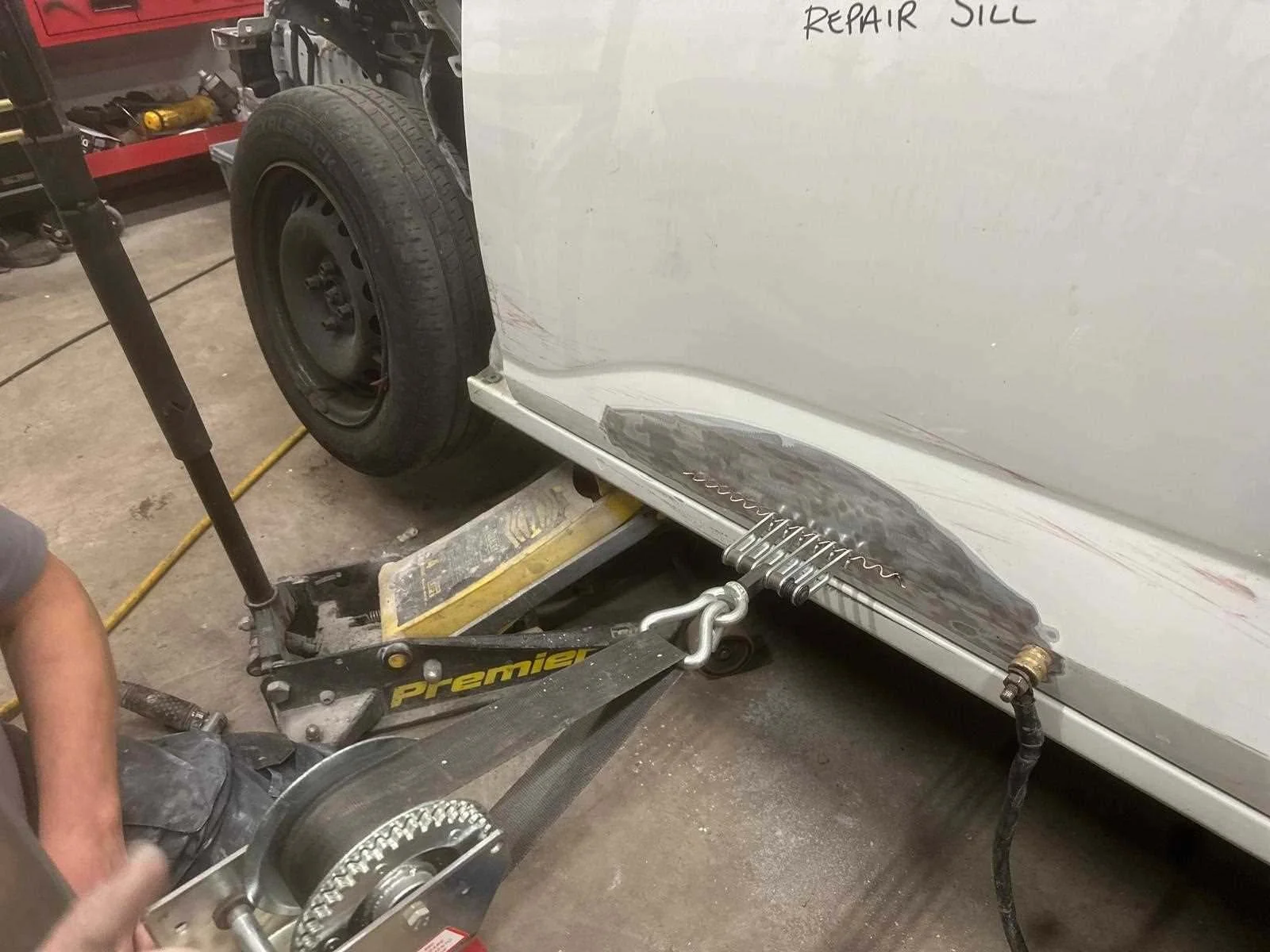 Dent pulling the lower section of a white Dacia Sandero. Car is jacked up and pins have been welded into the vehicle so that the dent can be safely pulled back into shape