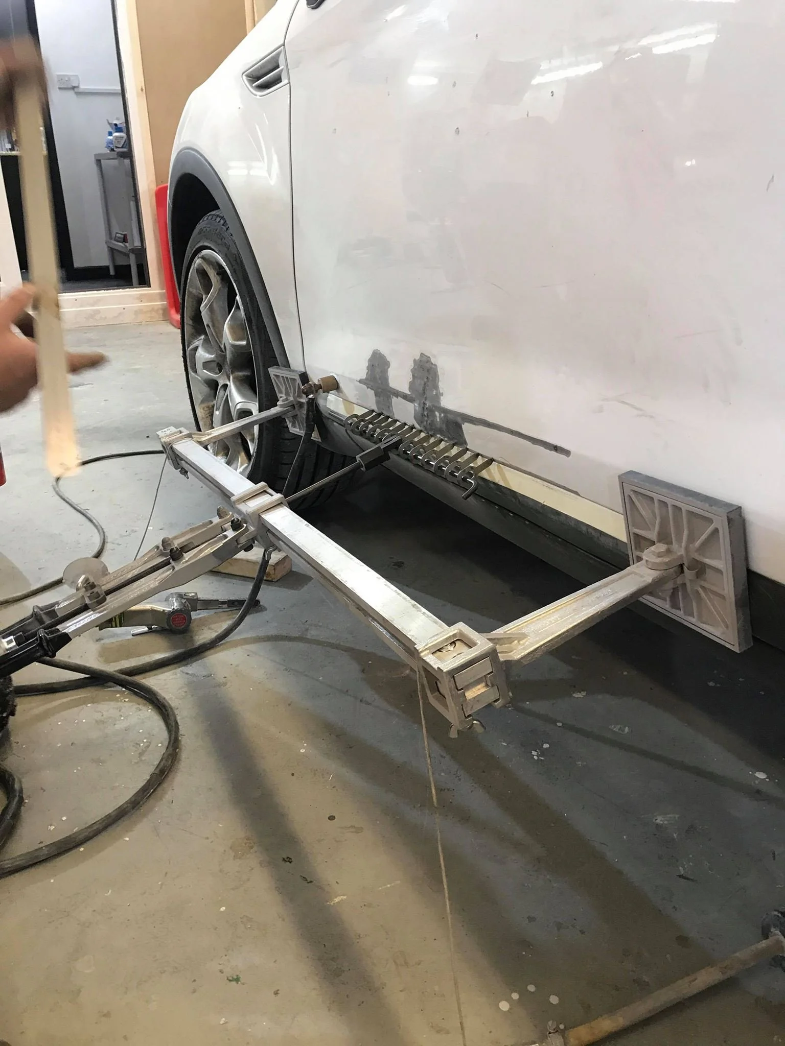 Car being measured or repaired in a garage, with a metal frame and measuring device attached to the side of the vehicle.