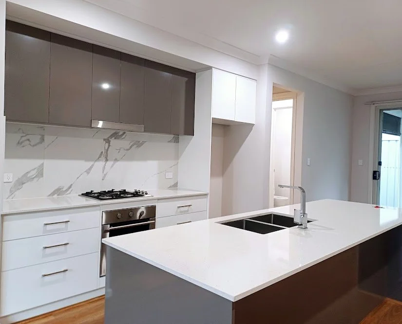 Modern kitchen with white cabinets, a marble backsplash, stainless steel oven and stove, and a white island with a sink.