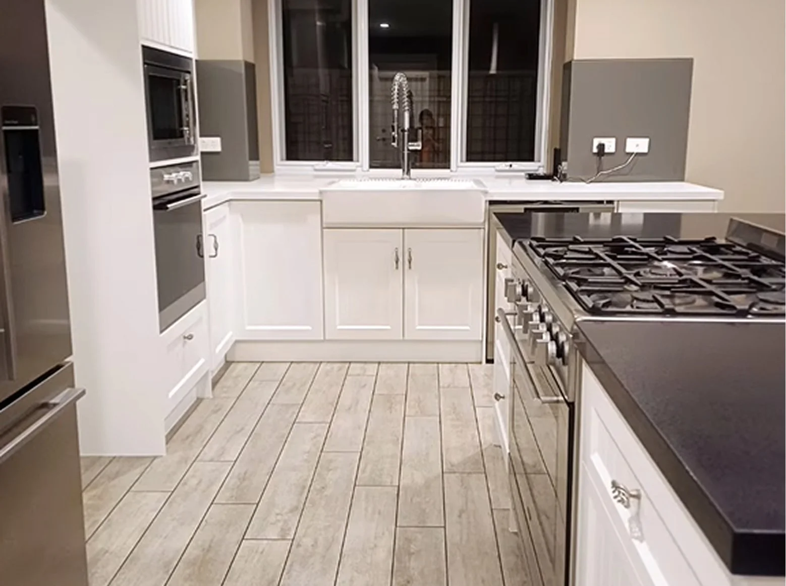 A modern kitchen with white cabinets, a black countertop, and a gas stove. There is a large window above the sink, and a microwave and oven built into the cabinetry.