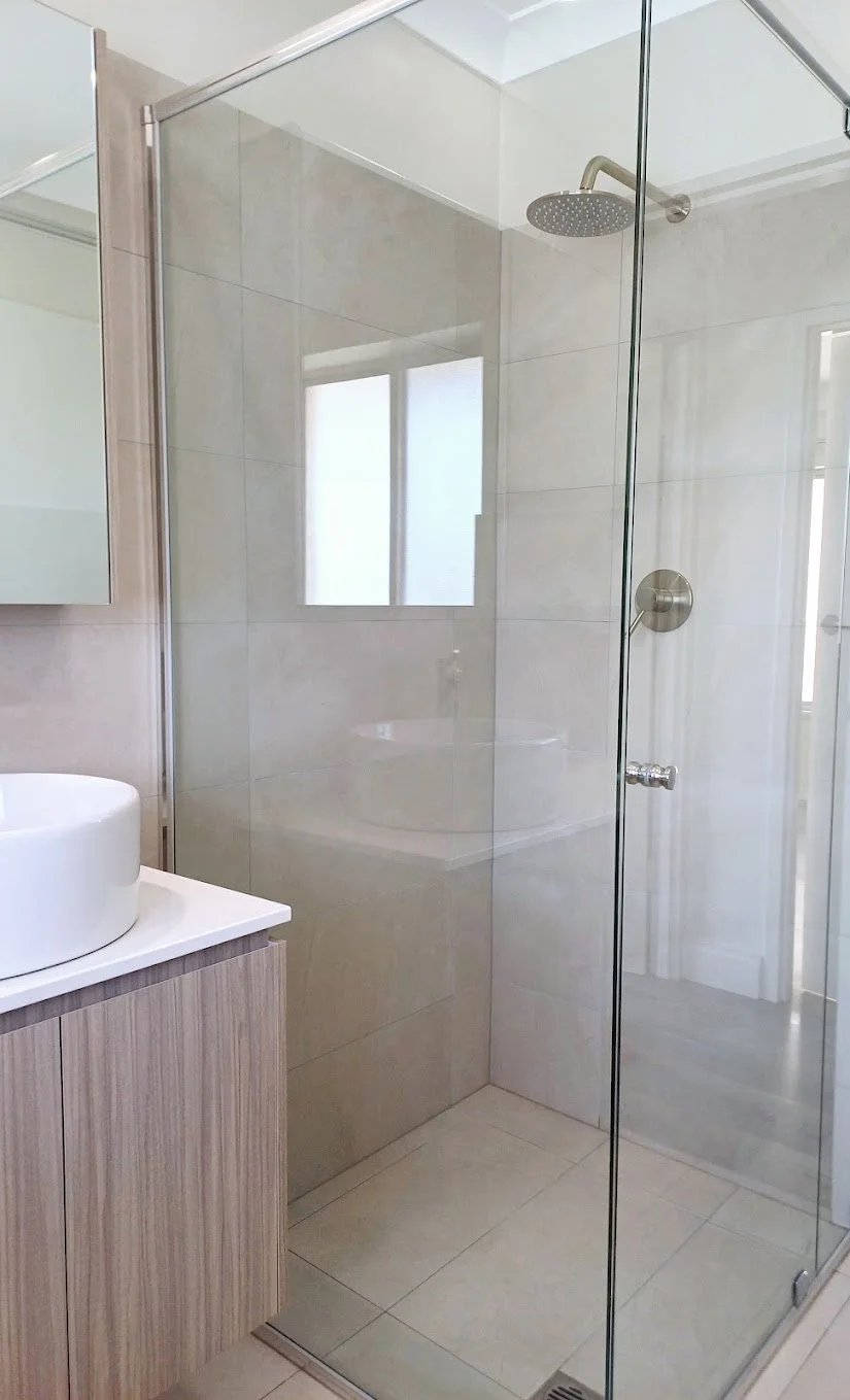 Modern bathroom with glass shower enclosure, rain showerhead, white vessel sink, and wooden vanity.
