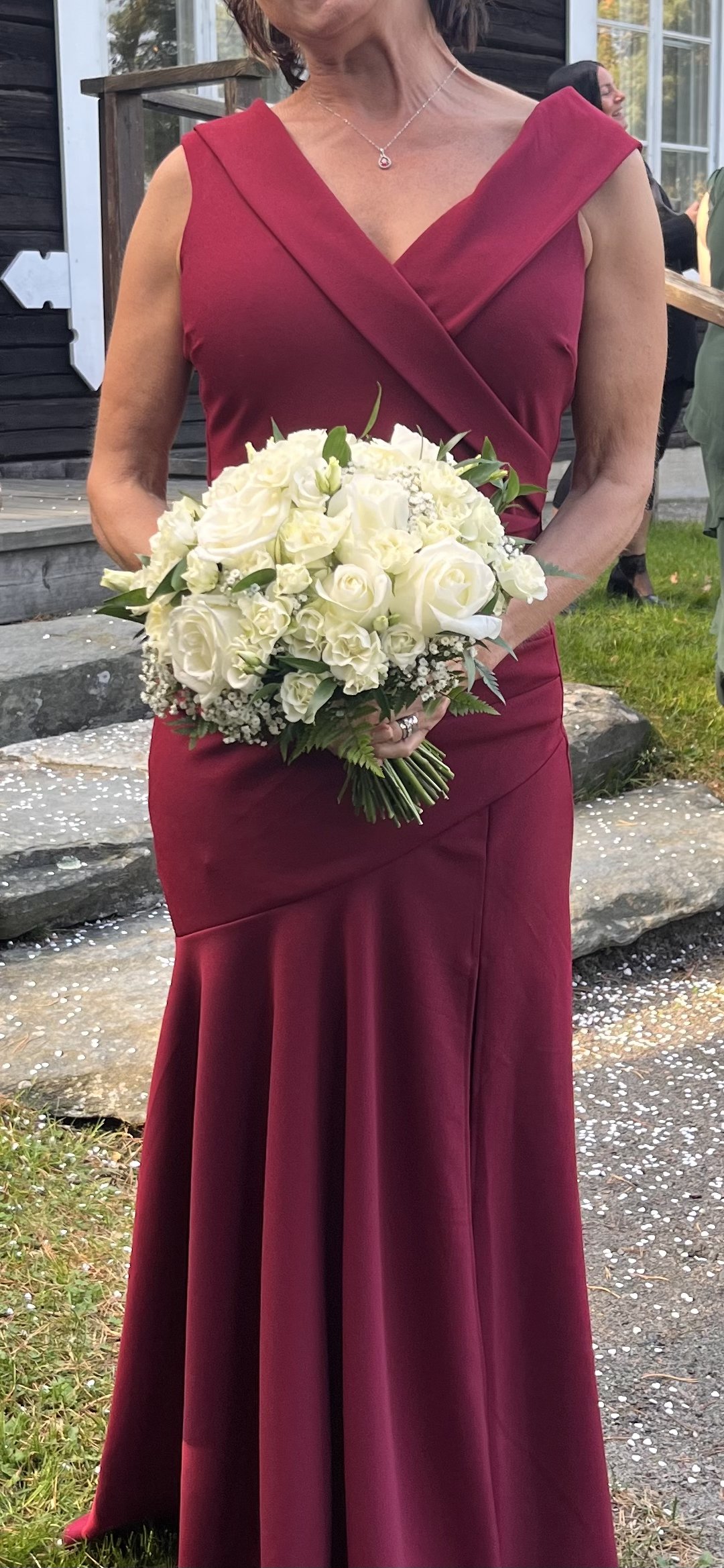 Kvinna i mörkröd klänning som håller en bukett med vita blommor.