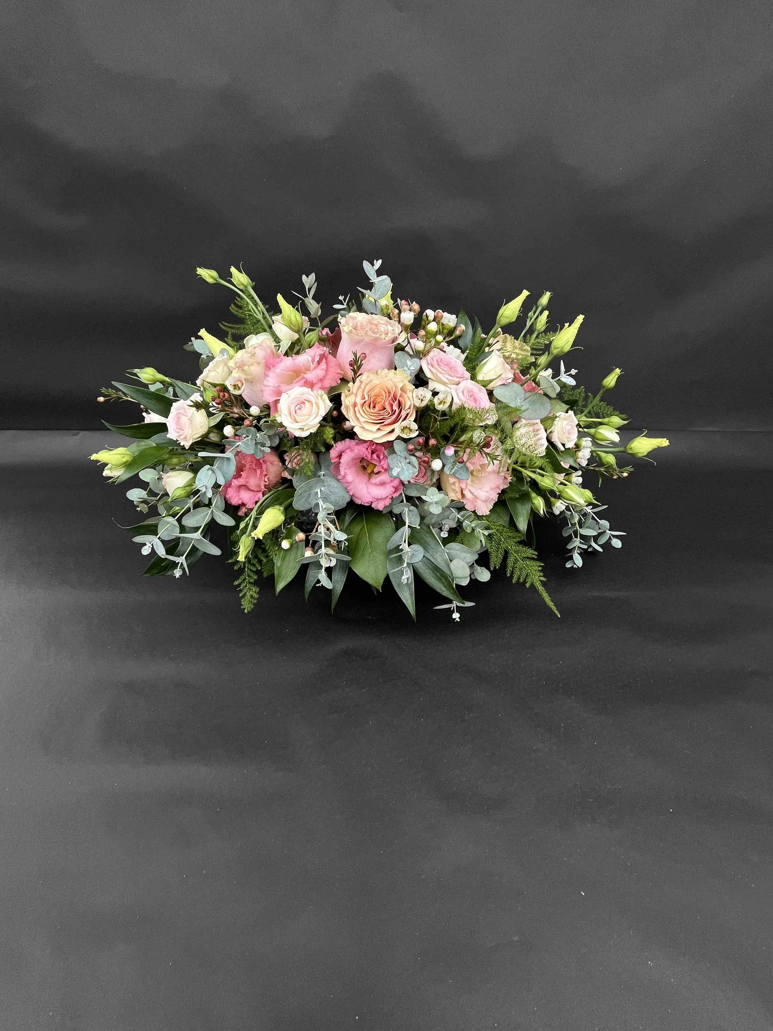 Färgglad blomsterarrangemang med rosa, vit och beige blommor på svart bakgrund.