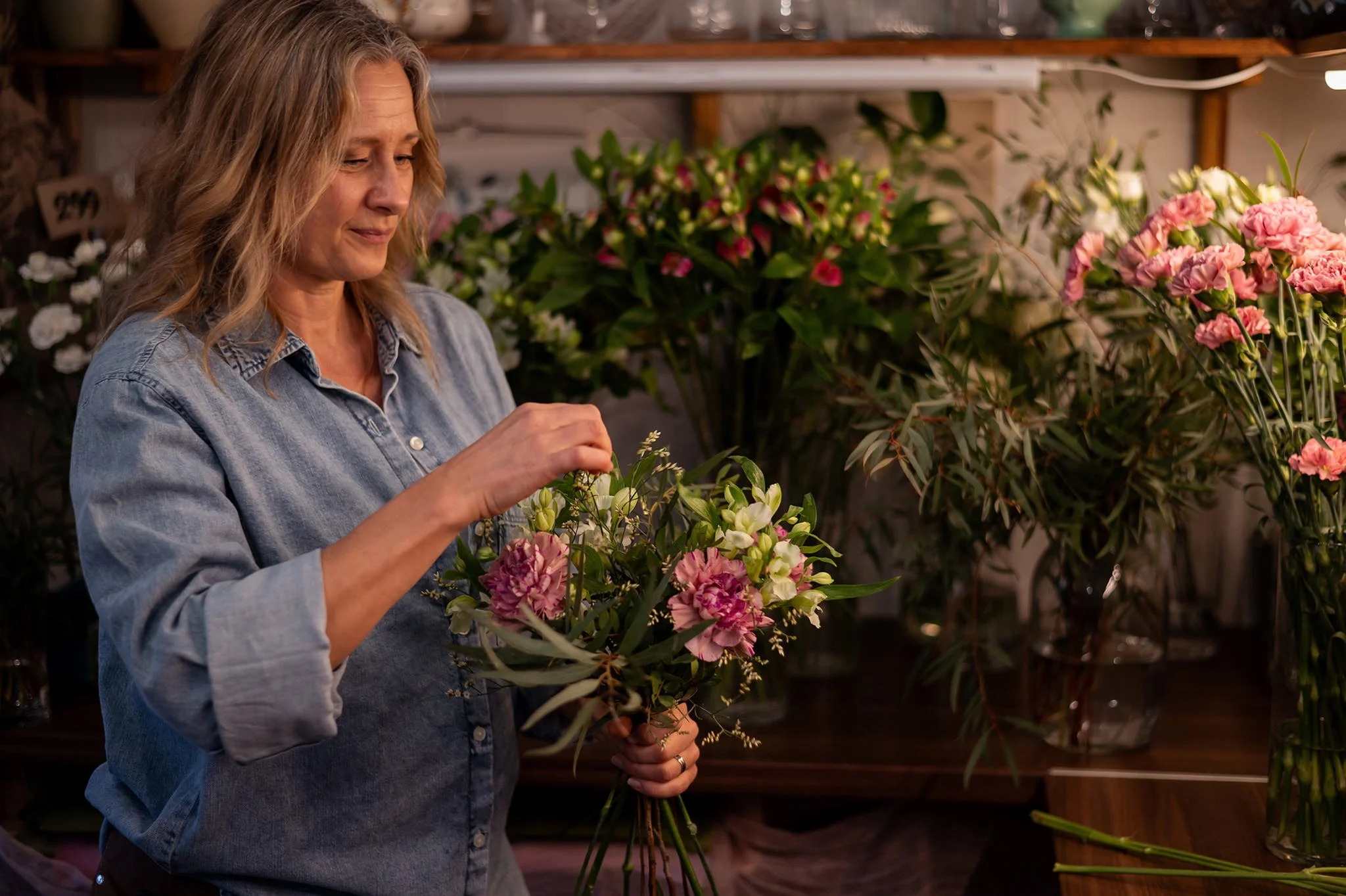 En florist som arbetar med att skapa en vacker bukett i en blomsterbutik, omgiven av olika blommor.