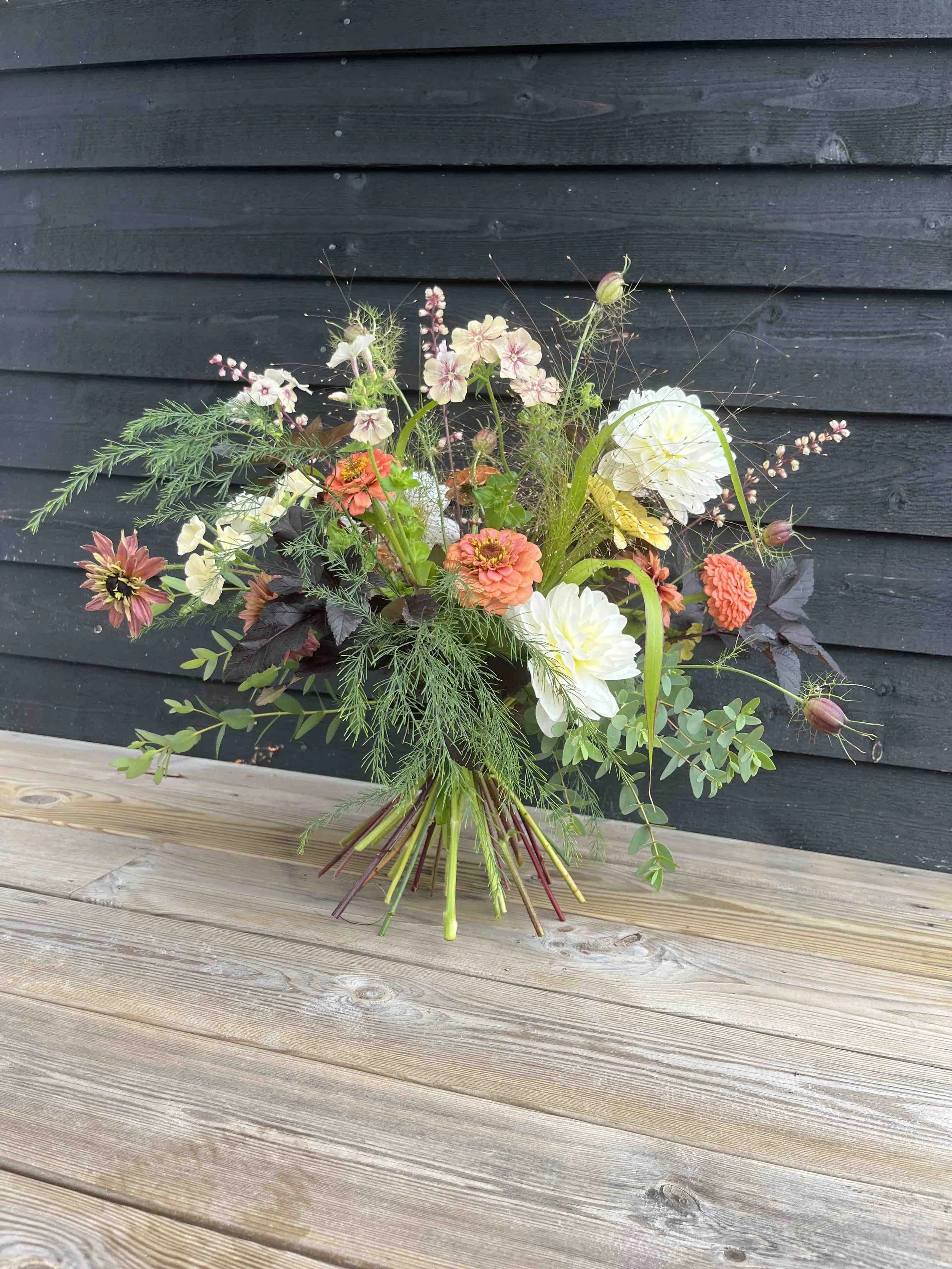 En  stående bukett med olika närodlade blommor i ljusa och mörka nyanser.