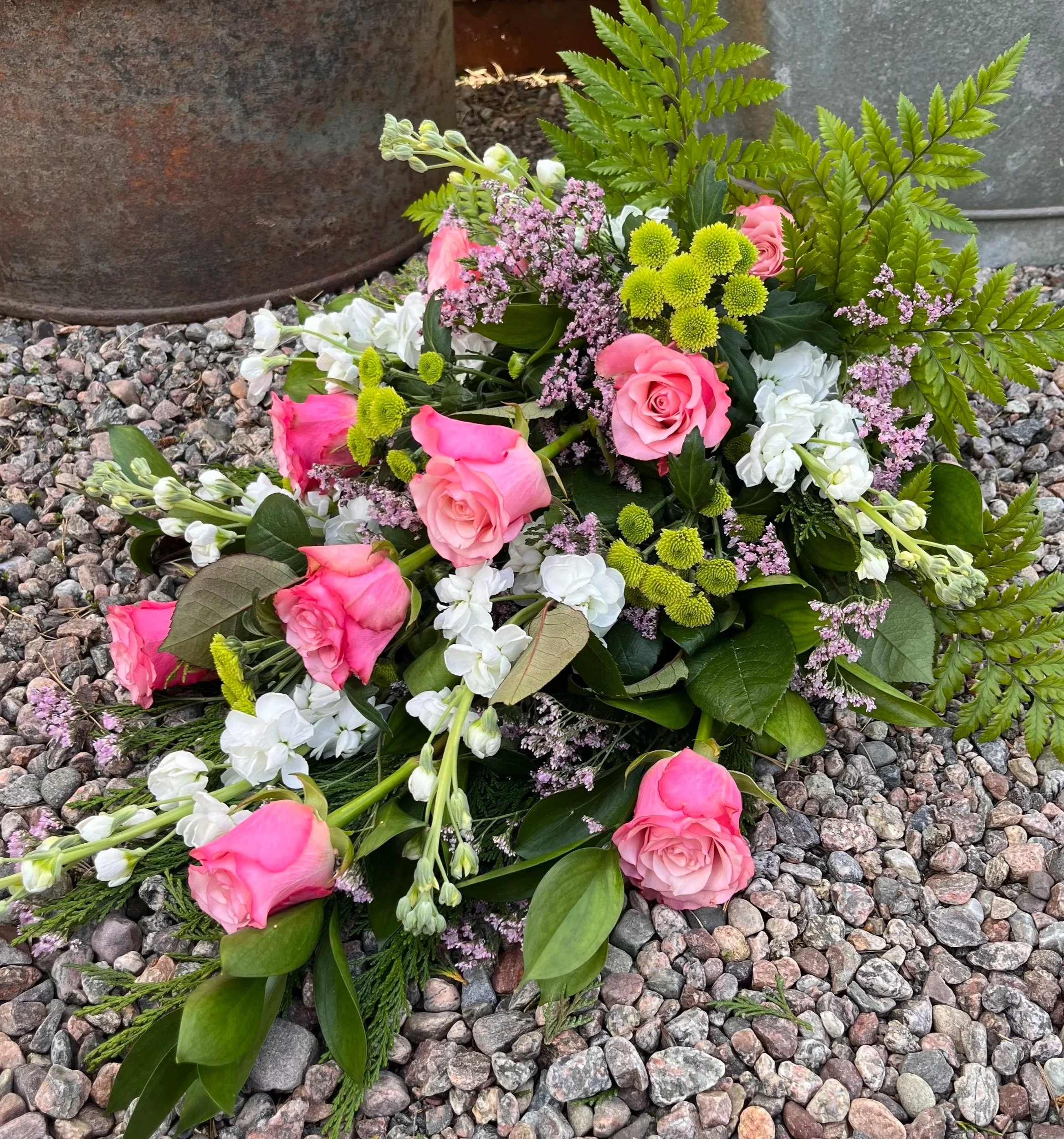 Begravningsblommor i rosa, vit och grönt, på en grusig yta