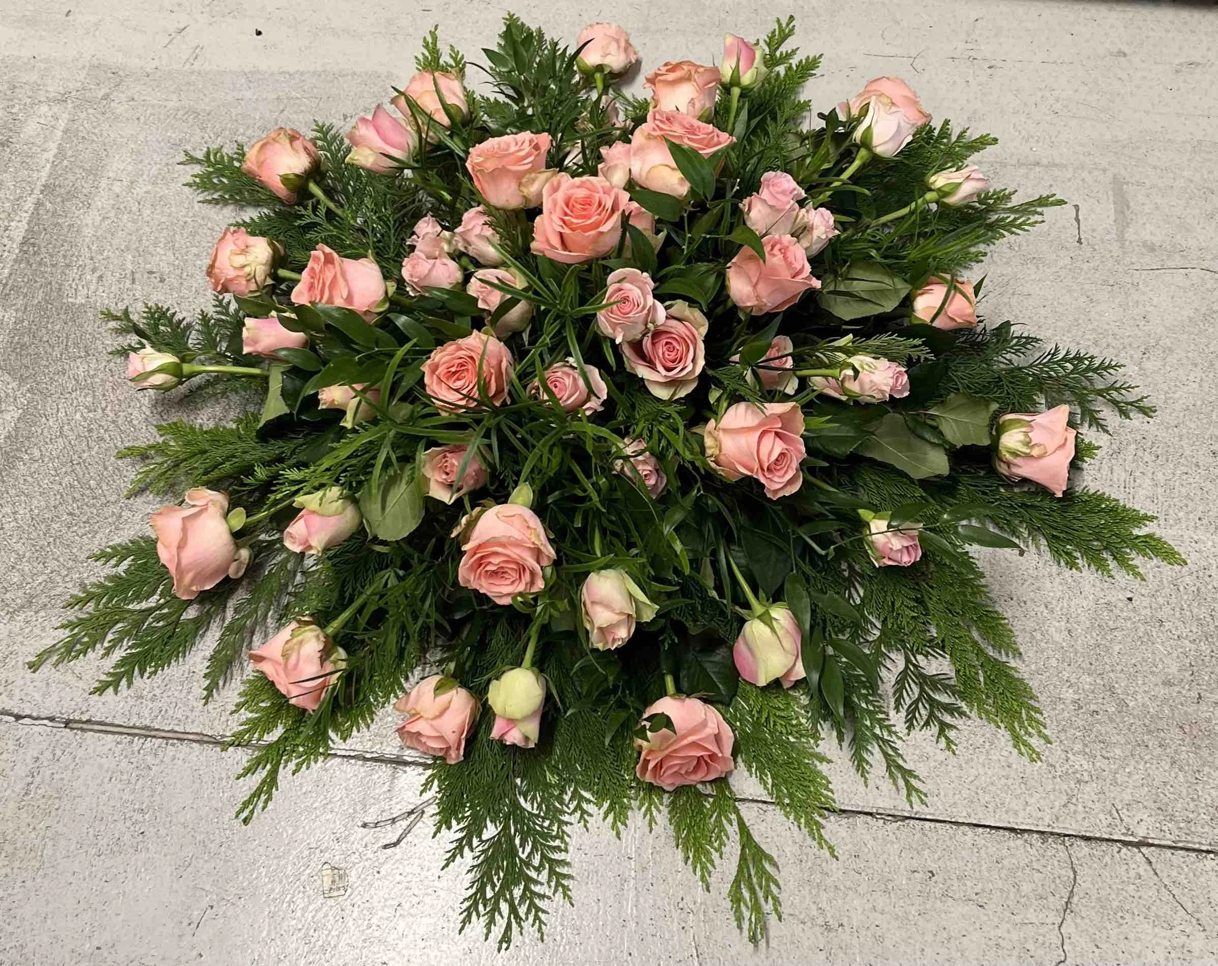 En rund, låg begravningsdekoration med rosa rosor och gröna blad.