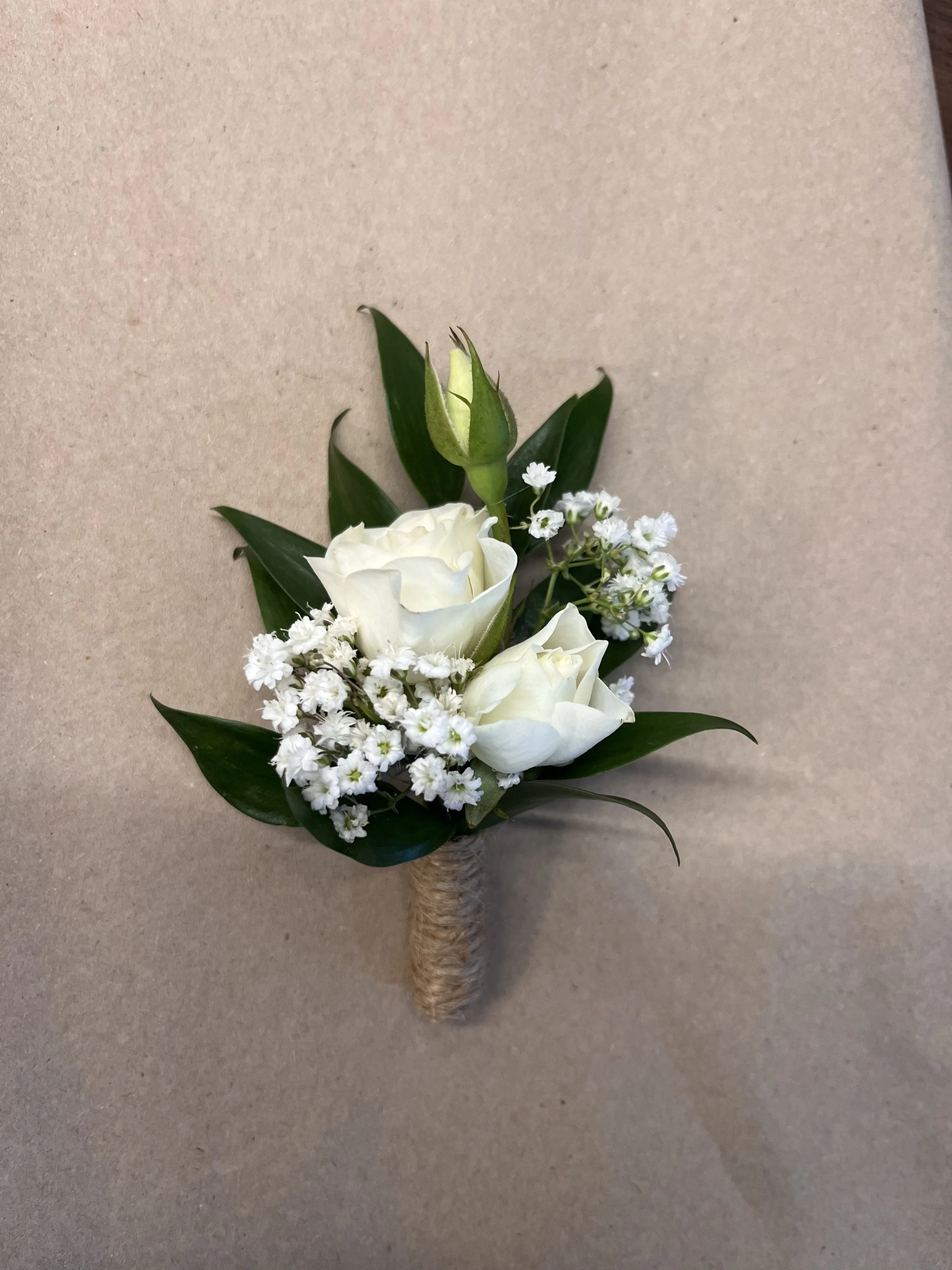 En annorlunda brudbukett med vita rosor, små vita blommor och gröna blad, med handtag lindat i jutesnöre.