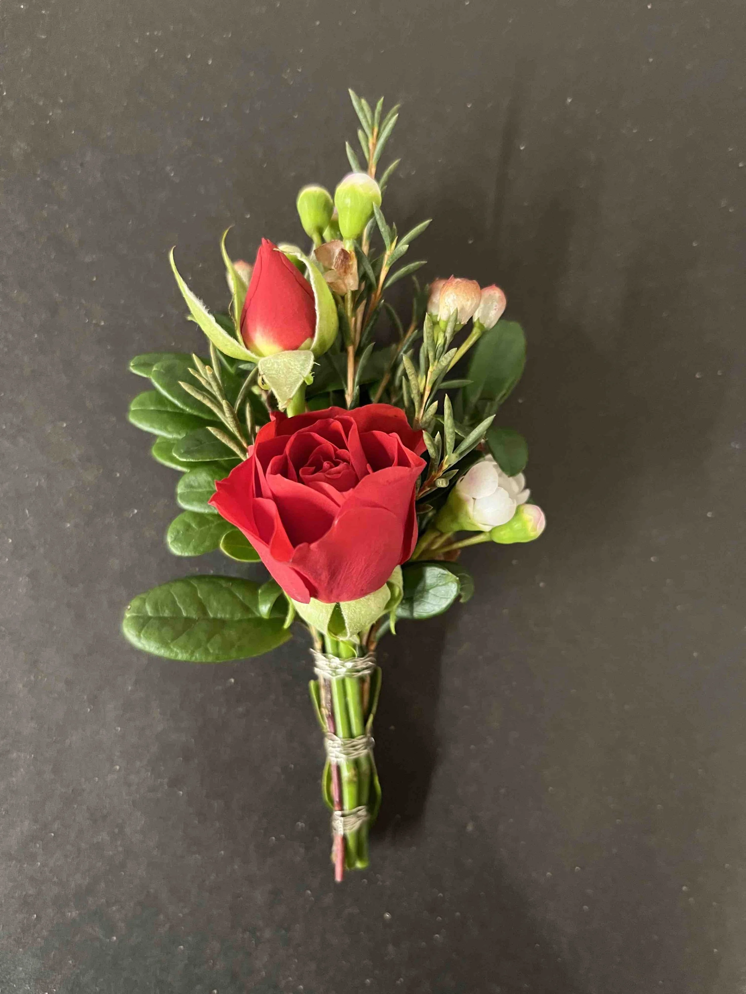 En liten blomsterbrud med röda och vita blommor, gröna blad och lagd på en svart bakgrund.