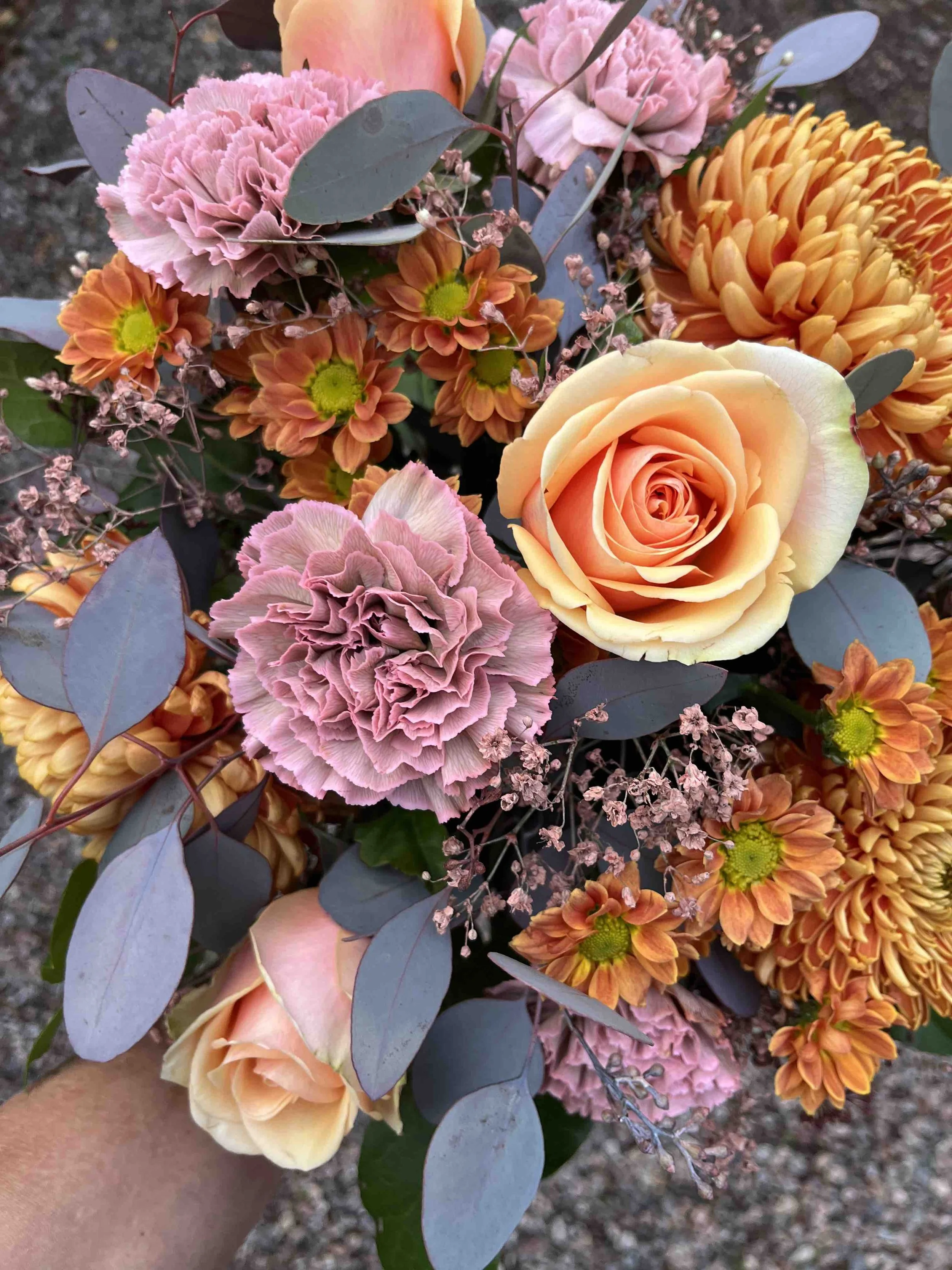 Blommig bukett med rosa, orange och aprikosfärgade blommor samt gröna och lila blad.