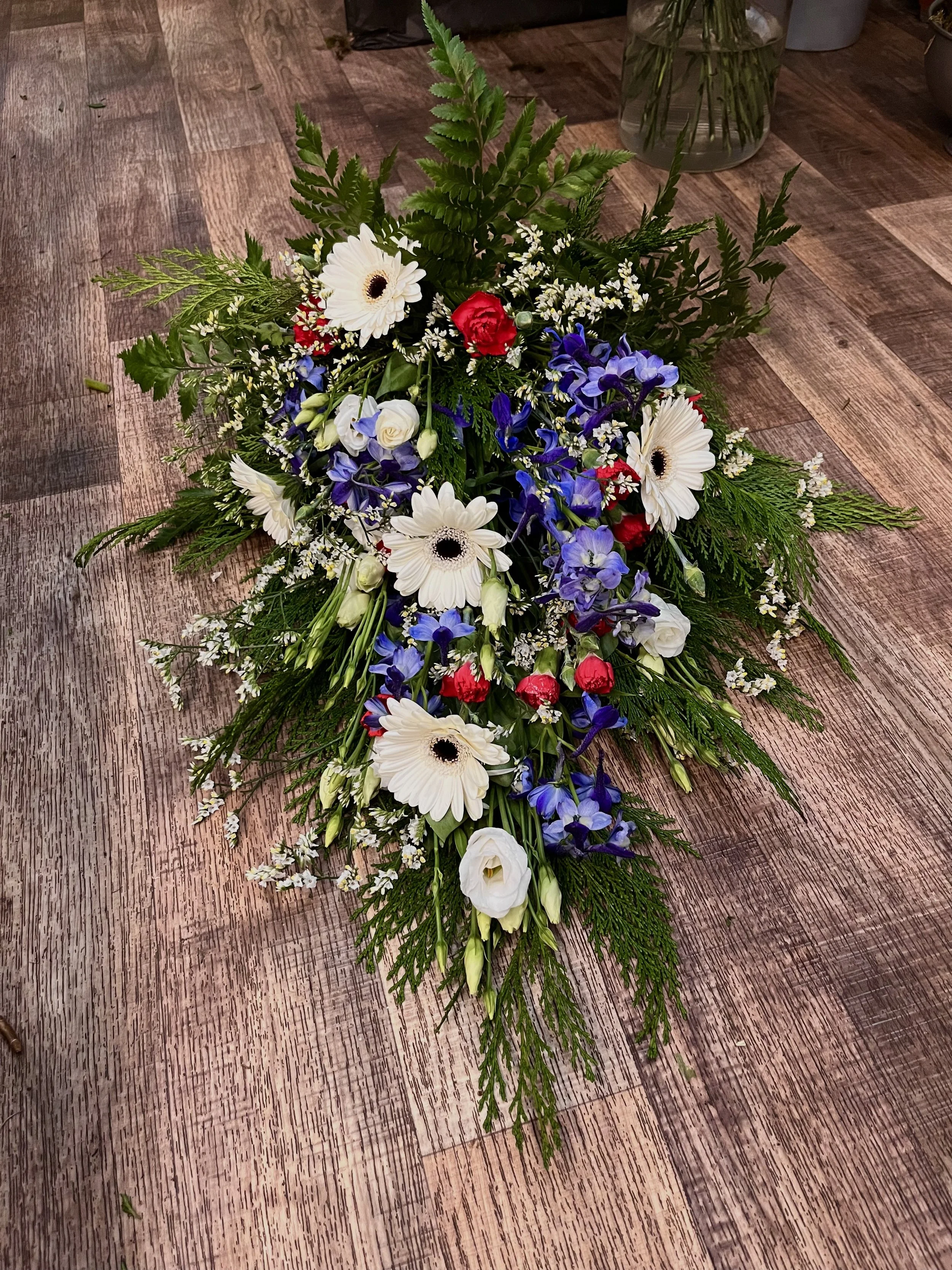 Begravningsblommor i vitt, blått, rött och grönt på ett träbord.