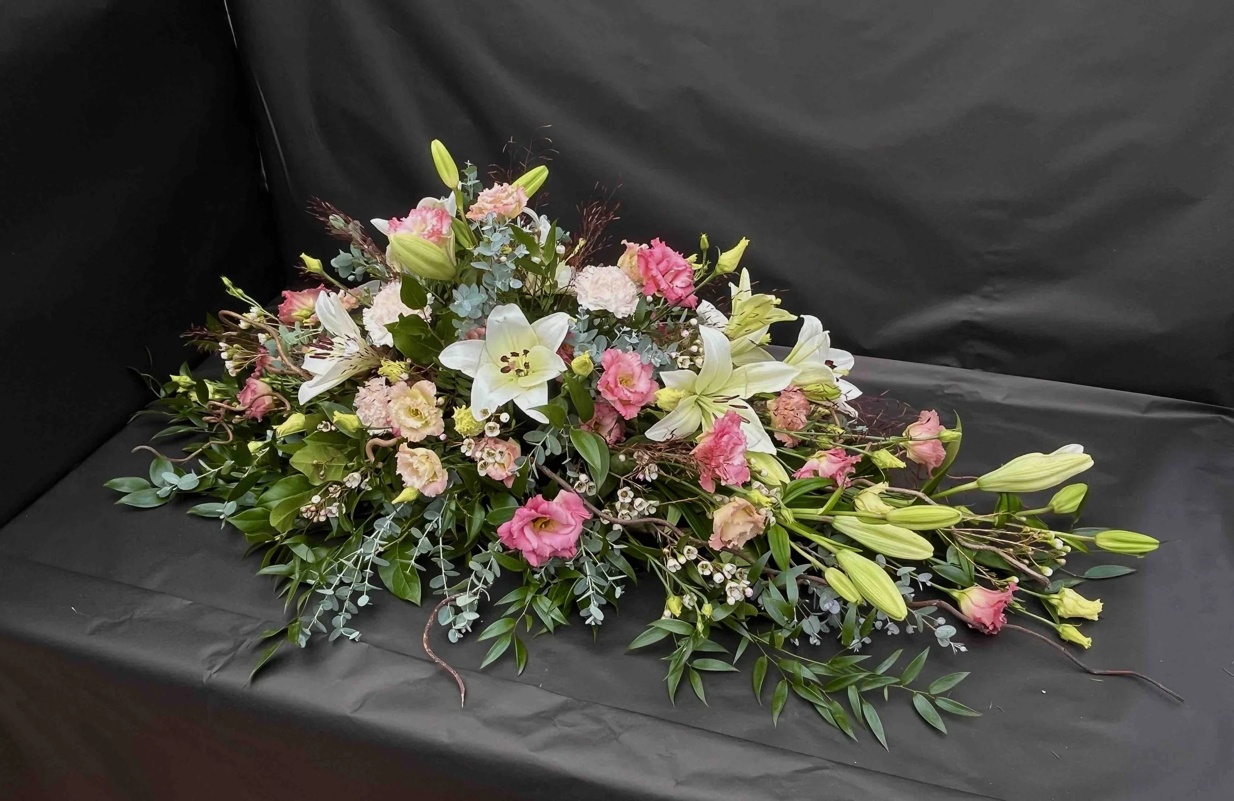 Kistdekoration med vita liljor och rosa blommor på svart bakgrund.