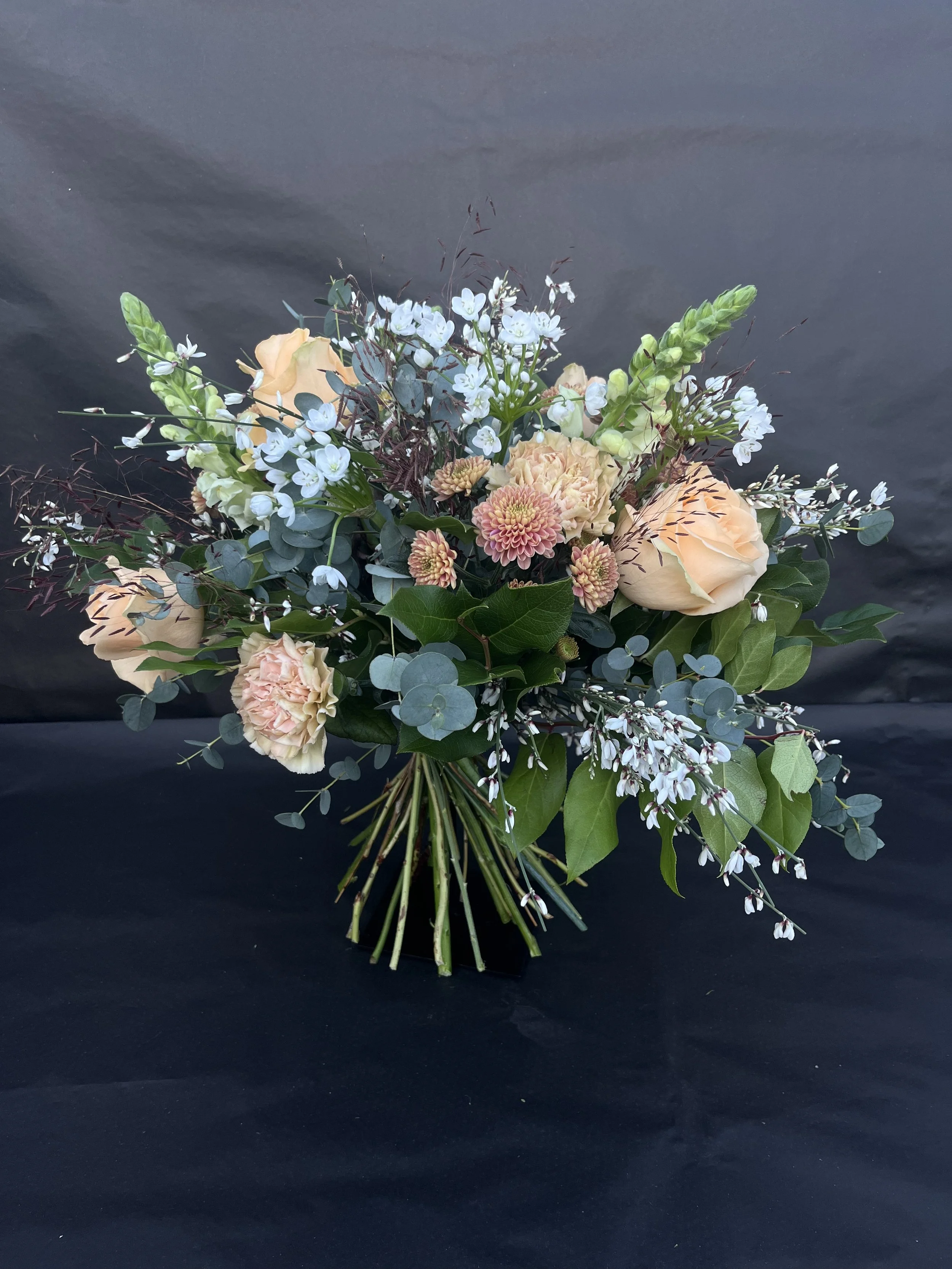 Blommig bukett med ljusrosa, beige och vita blommor samt gröna blad mot svart bakgrund.