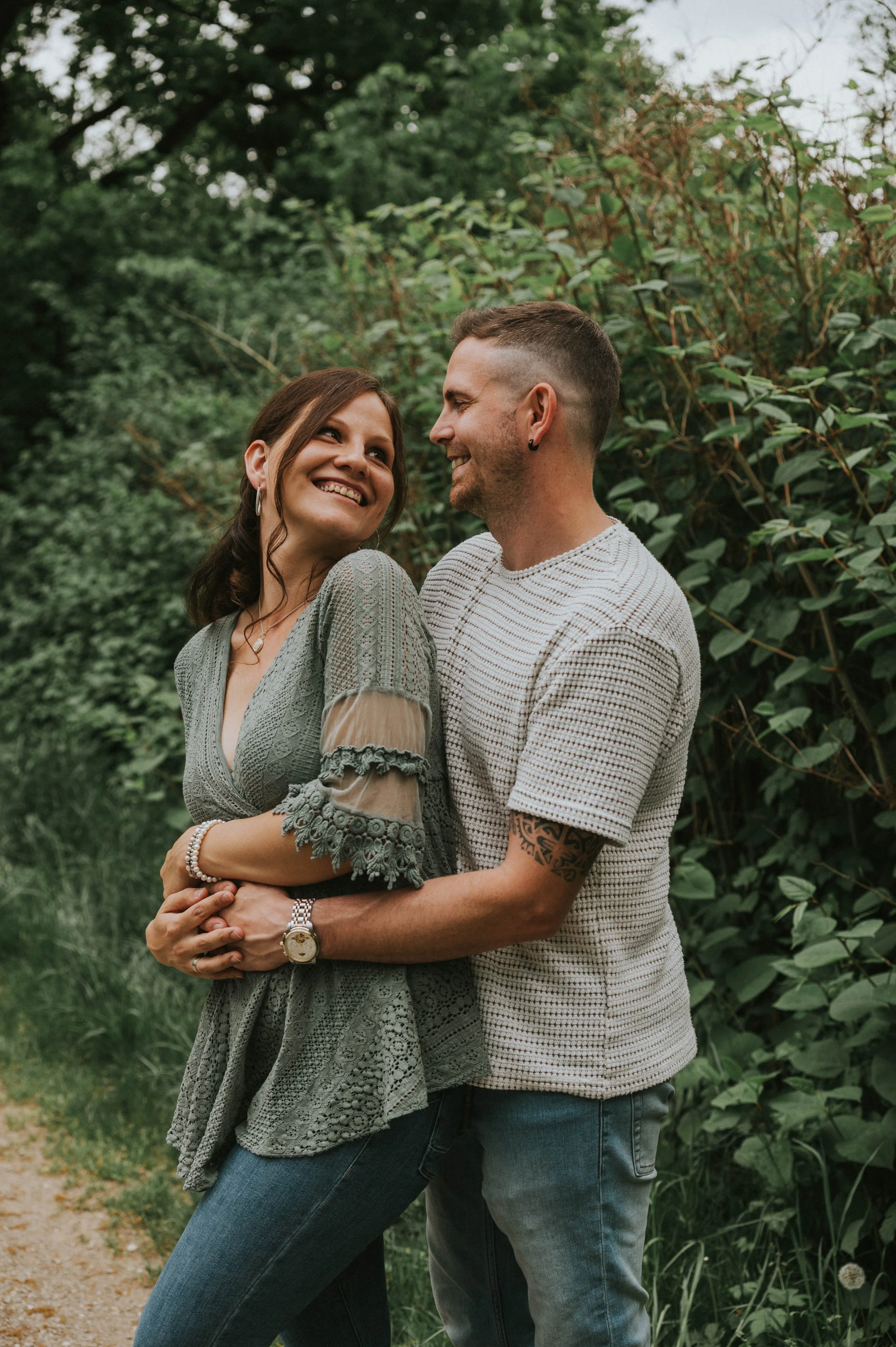 Ein glückliches Paar, das sich umarmt und sich anlächelt, in einer grünen Naturumgebung im Freien.