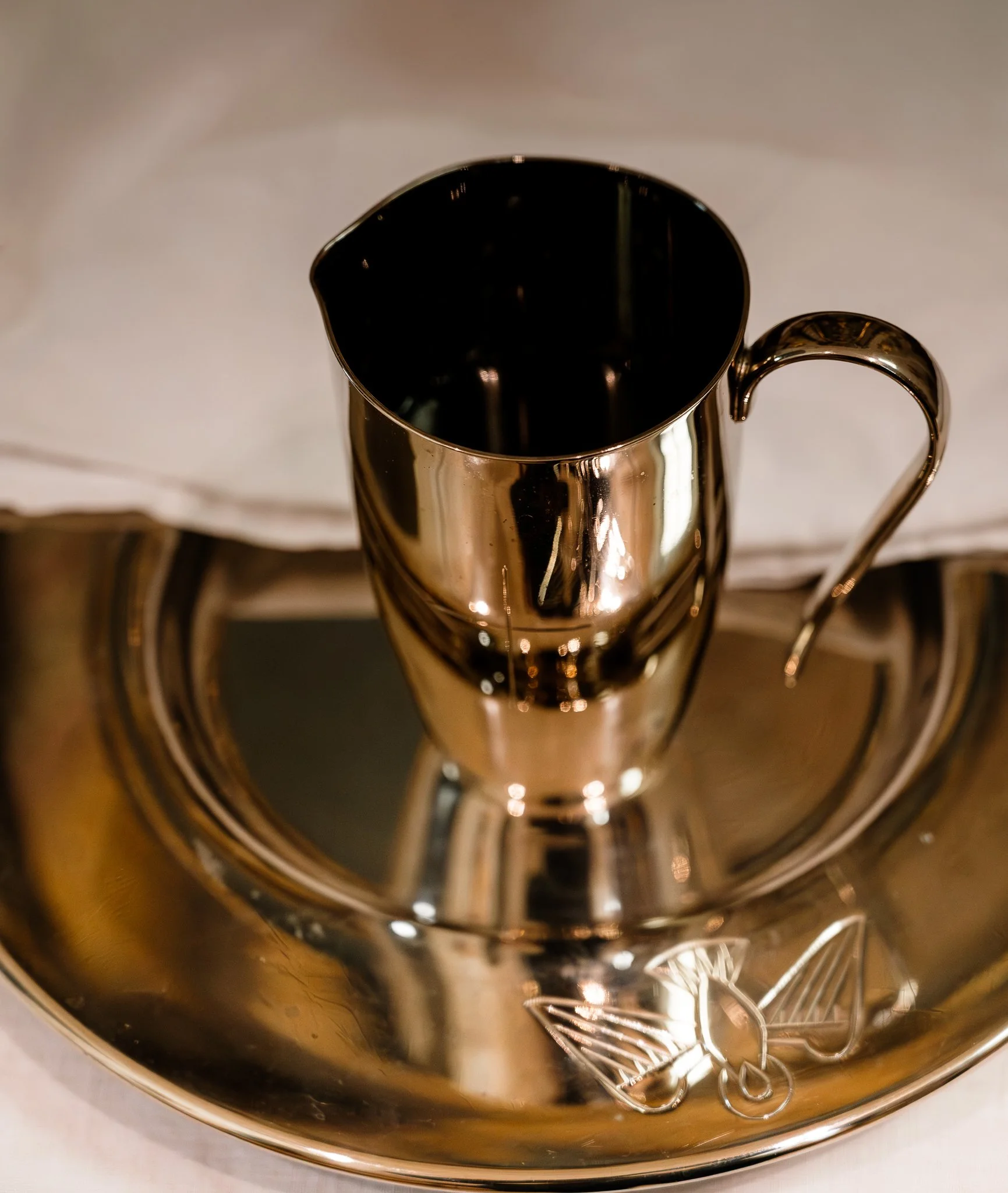 Ein silberner Kaffeekrug auf einem runden silbernen Tablett, auf dem auch eine dekorative Schleife liegt.