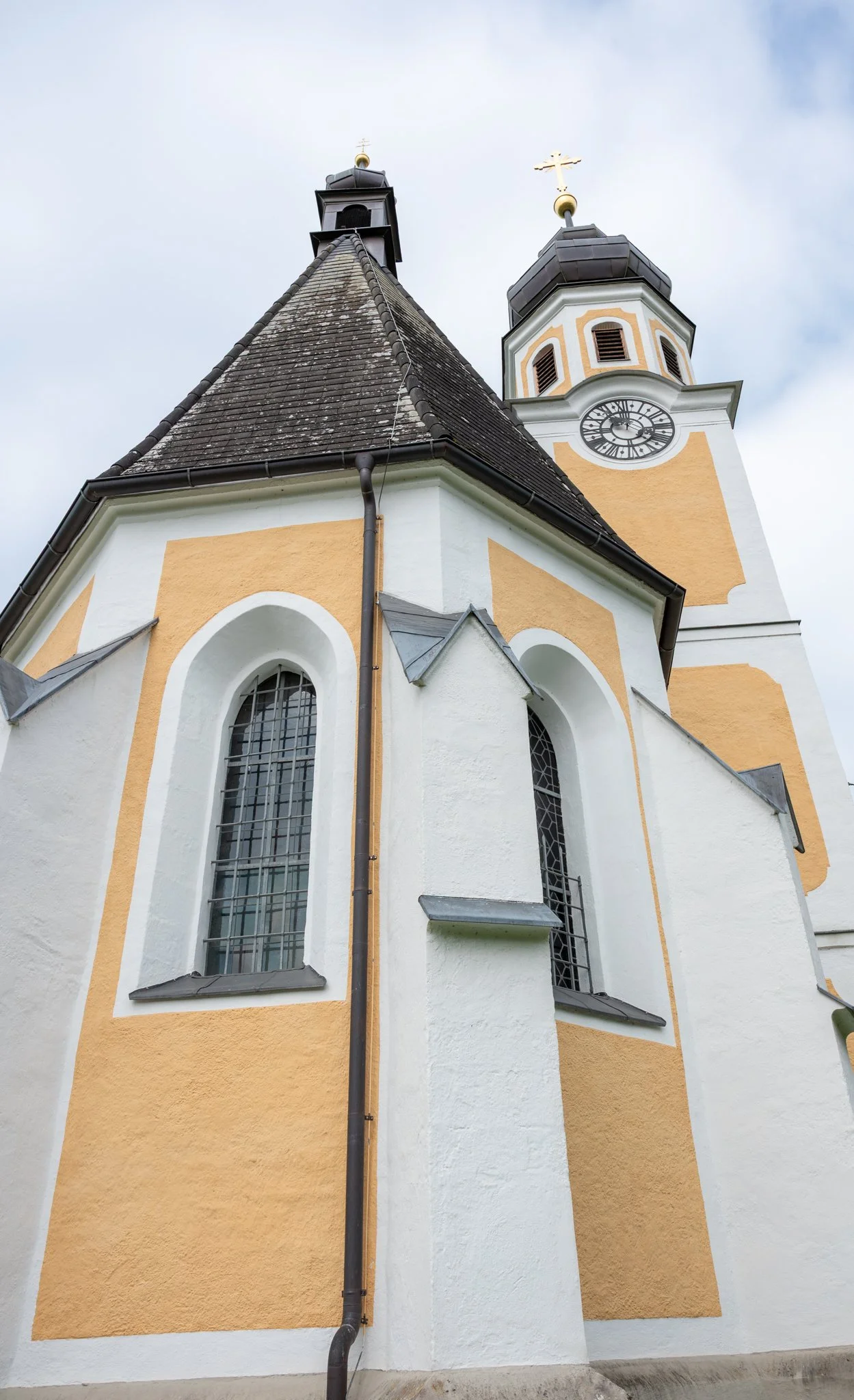 Eine Kirche mit gelben und weißen Wänden, hohen fenstern und einem Uhren-Zeitanzeiger an der Turmuhr, sowie einem Kreuz auf der Spitze des Kirchturms.