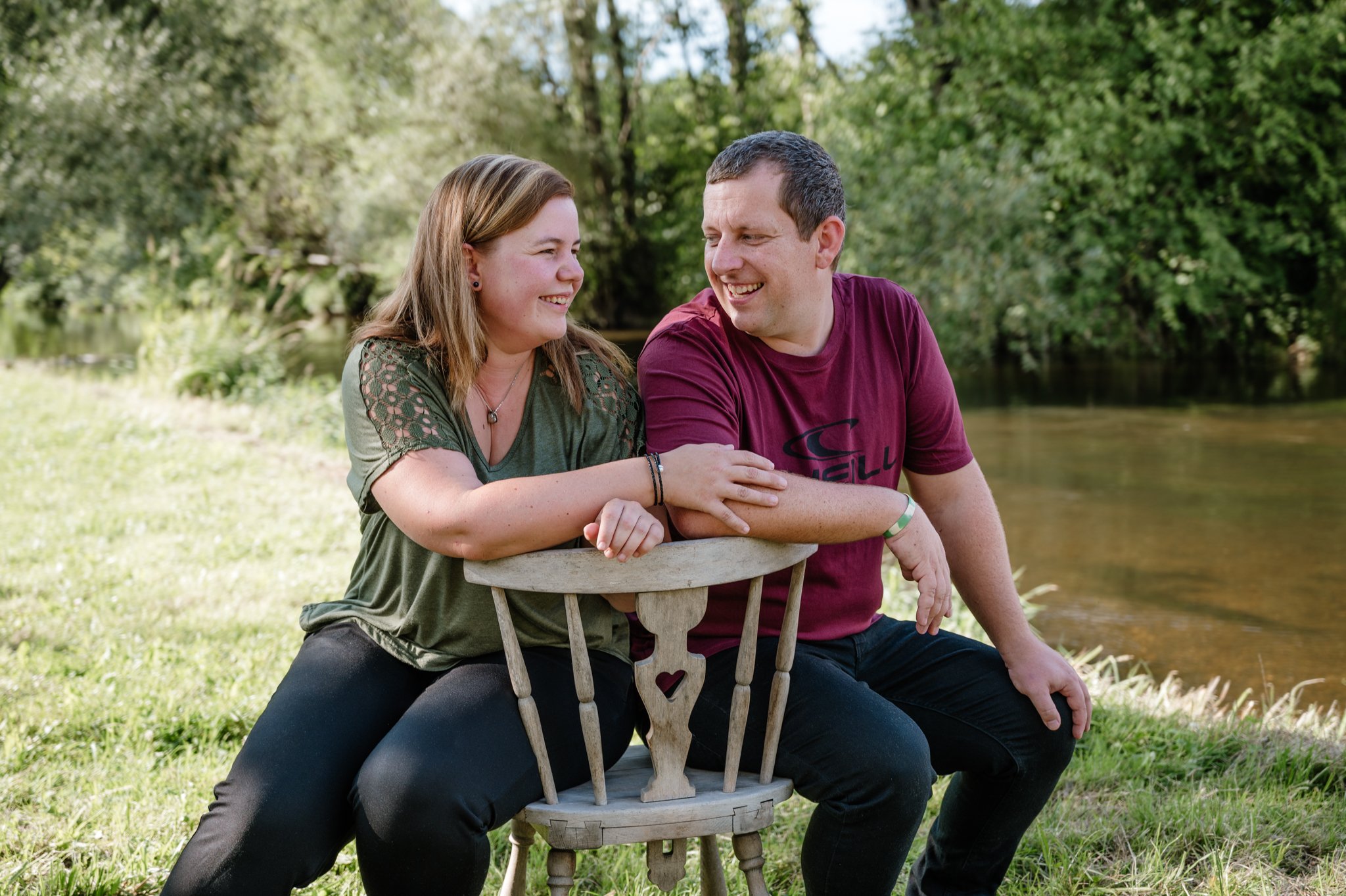 Ein lachendes Paar sitzt draußen an einem See, umgeben von Bäumen, und teilt einen Moment der Freude.