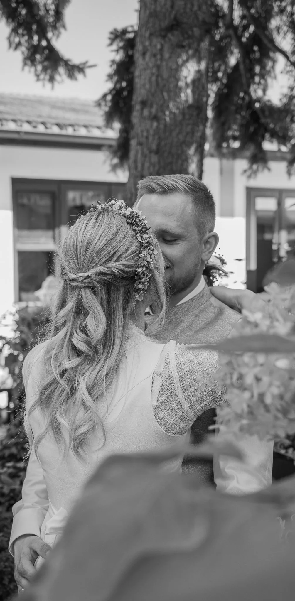 Ein Brautpaar bei einer Hochzeit, umarmend und innig küsset, draußen vor einem Baum, in Schwarz-Weiß aufgenommen.